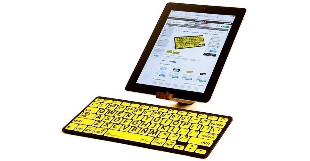 Tablet auf einem Ständer zeigt eine Webseite. Eine gelbe Tastatur mit großen, schwarzen Buchstaben ist vor dem Tablet platziert.