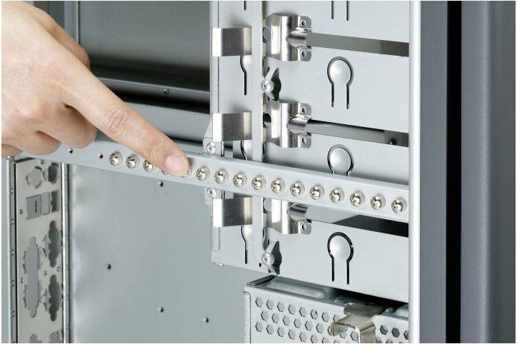 'Eine Hand zeigt auf eine Reihe von Schrauben an der Innenseite eines Computergehäuses, fokussiert auf die Befestigungselemente.'