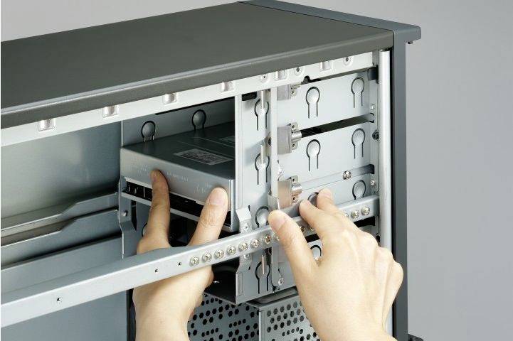 Person installiert eine Festplatte in einem Computergehäuse. Hände halten die Festplatte, während sie in den Schacht geschoben wird.