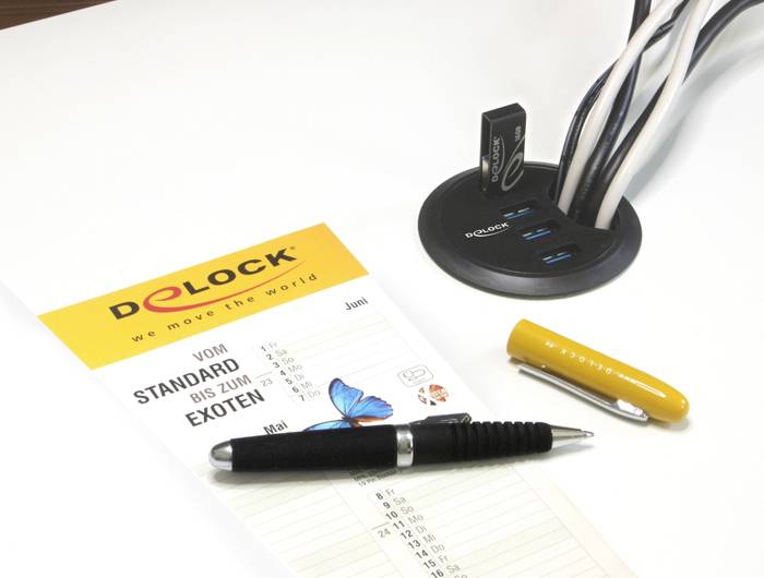 Ein Tisch mit einem Katalog, einem Kugelschreiber und einem USB-Hub mit mehreren Kabeln. Der Katalog trägt den Titel 'Von Standard bis zum Exoten'.