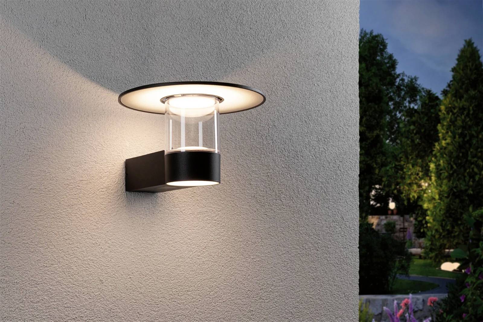 Außenwandleuchte an beigem Gebäude, beleuchtet Umgebung in der Abenddämmerung.