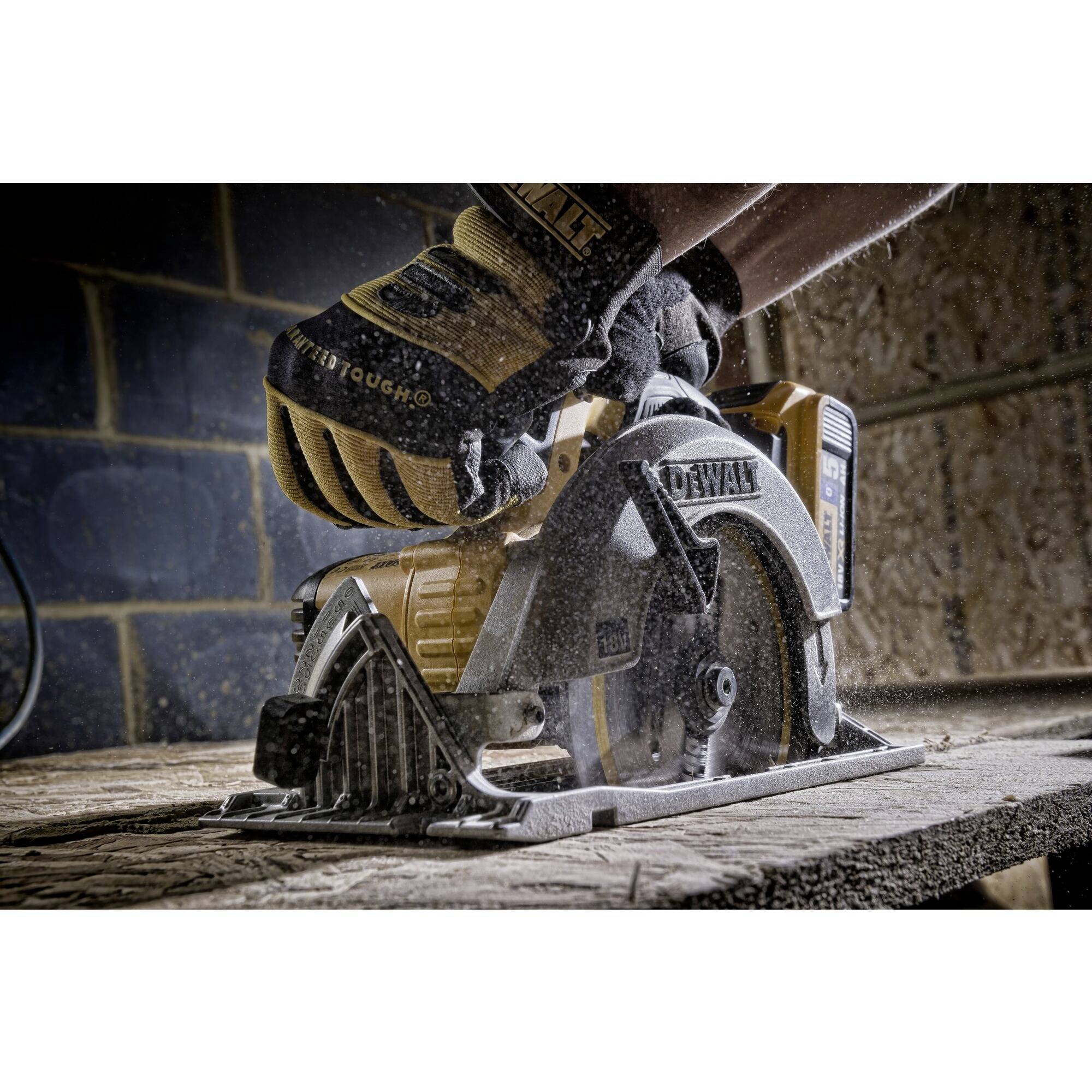 Eine Hand sägt mit einer elektrischen Kreissäge Holz auf einer Baustelle, während Schutzkleidung getragen wird.