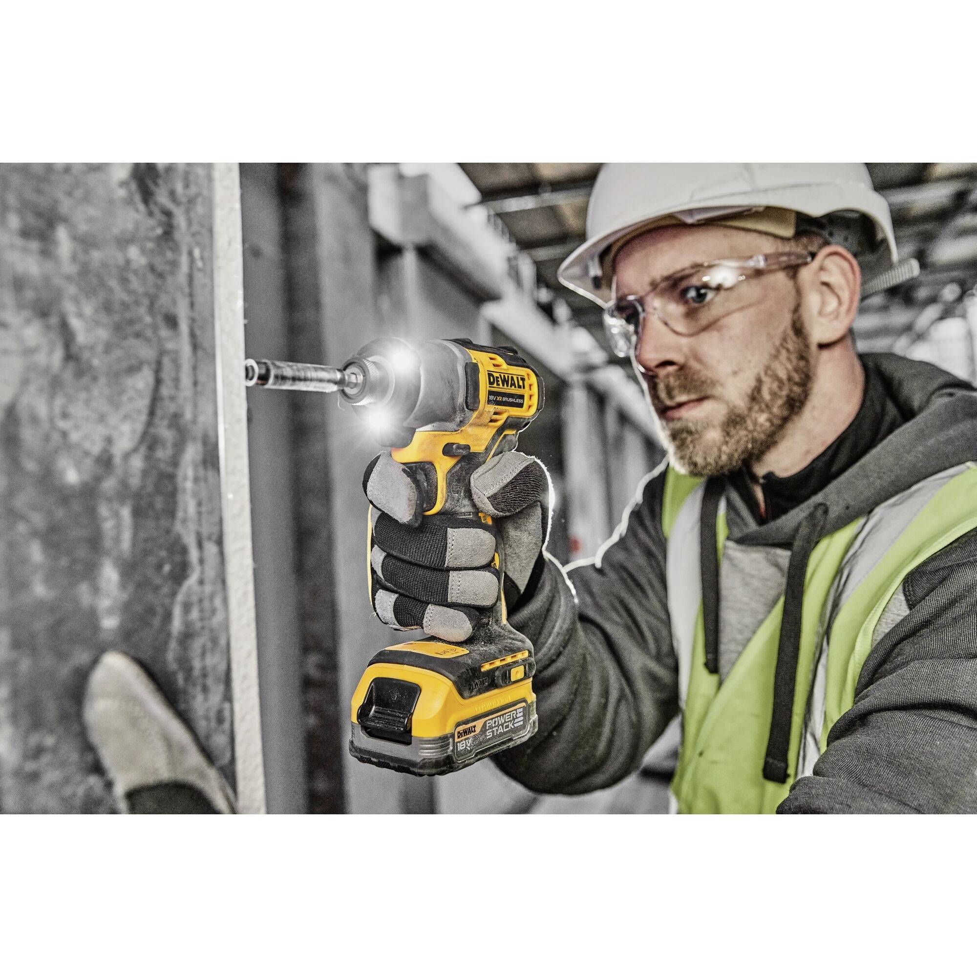 Arbeiter trägt Helm und Schutzbrille, benutzt einen Bohrer für Bauarbeiten an einer Betonwand in einer industriellen Umgebung.