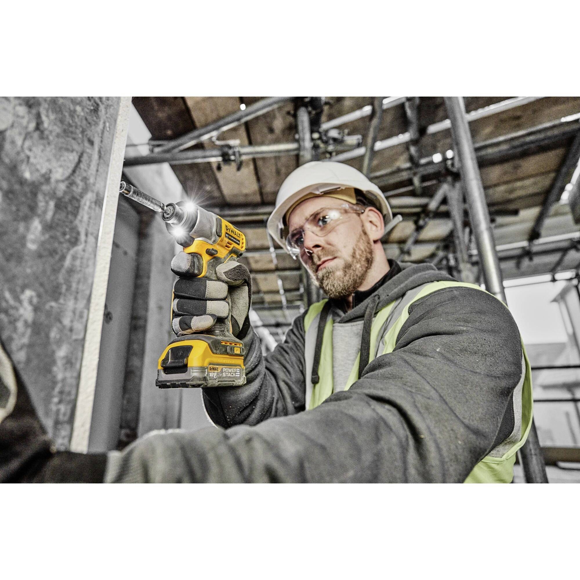 Ein Bauarbeiter mit Schutzhelm und Sicherheitsweste bohrt mit einem Akku-Bohrer in Beton auf einer Baustelle.