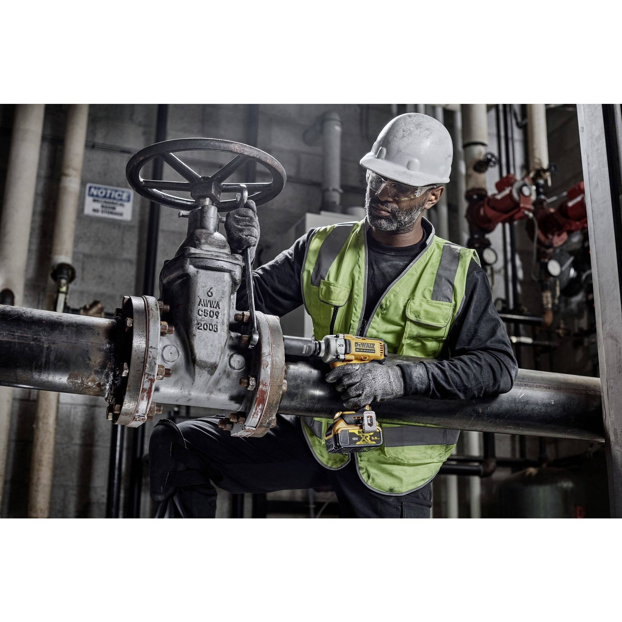 Ein Arbeiter in Schutzkleidung betätigt ein Ventil an einer großen Rohrleitung in einer industriellen Umgebung.