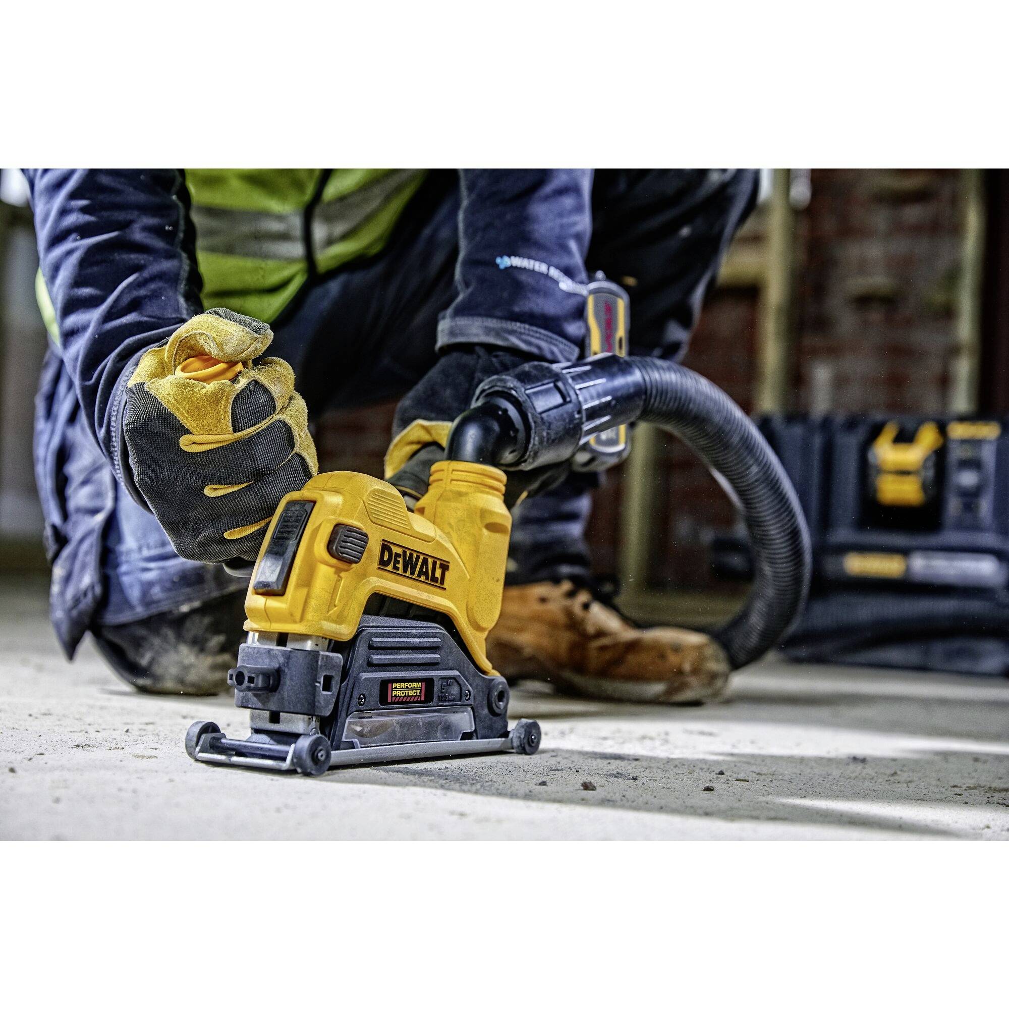 Ein Arbeiter nutzt einen Elektroschleifer von Dewalt, trägt Sicherheitskleidung und Handschuhe, während er auf einem Betonboden arbeitet.