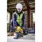 Eine Person in Schutzkleidung und Helm verwendet ein Werkzeug in einem Gebäuderohbau. Der Fokus liegt auf der Arbeitssituation.