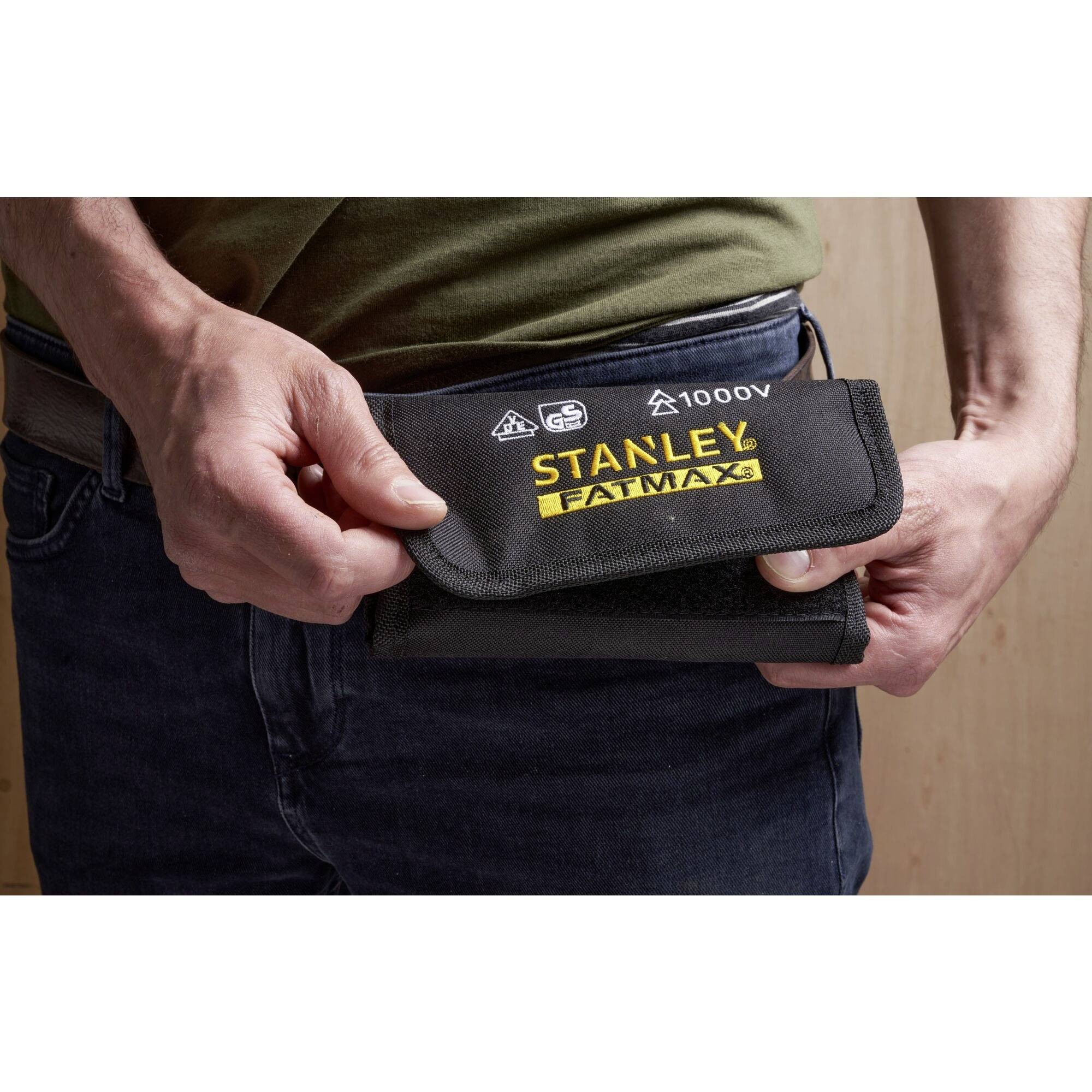 Eine Person steckt eine schwarze Stanley Fatmax-Tasche in die Hosentasche. Die Tasche enthält Werkzeuge und ist für bis zu 1000V isoliert.