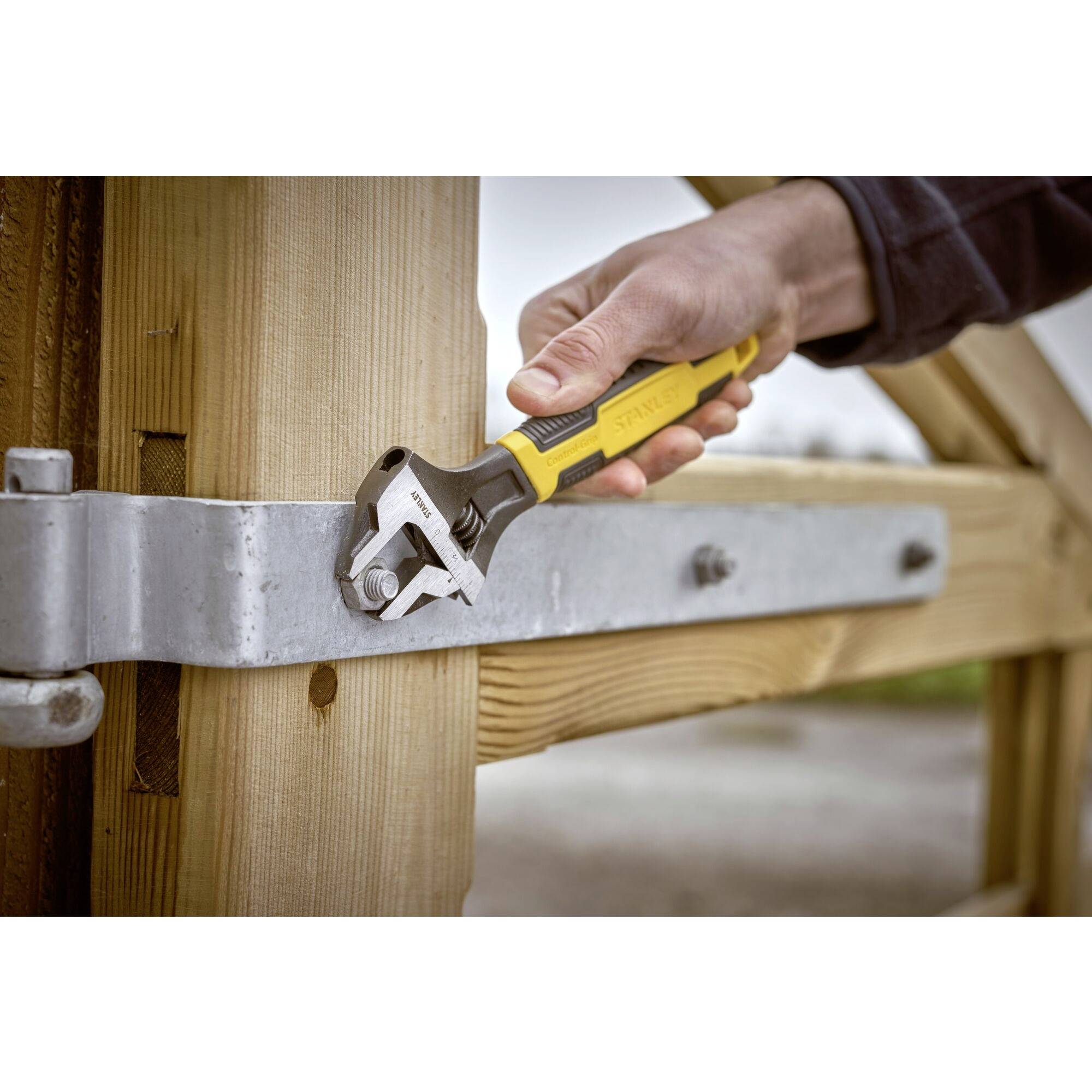 'Hand zieht Schraube mit verstellbarem Schraubenschlüssel an, befestigt Metallbeschlag an Holztorrahmen im Freien.'