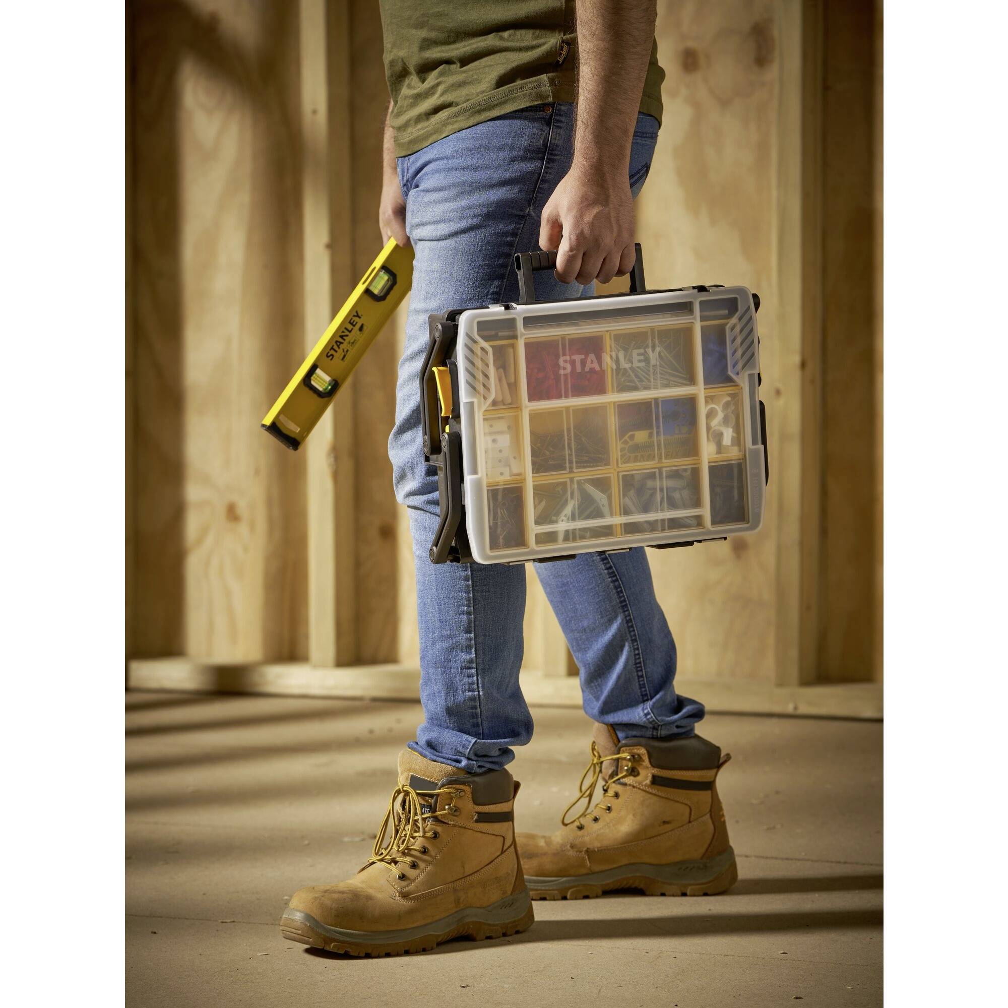 Eine Person hält eine Werkzeugbox und eine Wasserwaage in einer Holzwerkstatt.