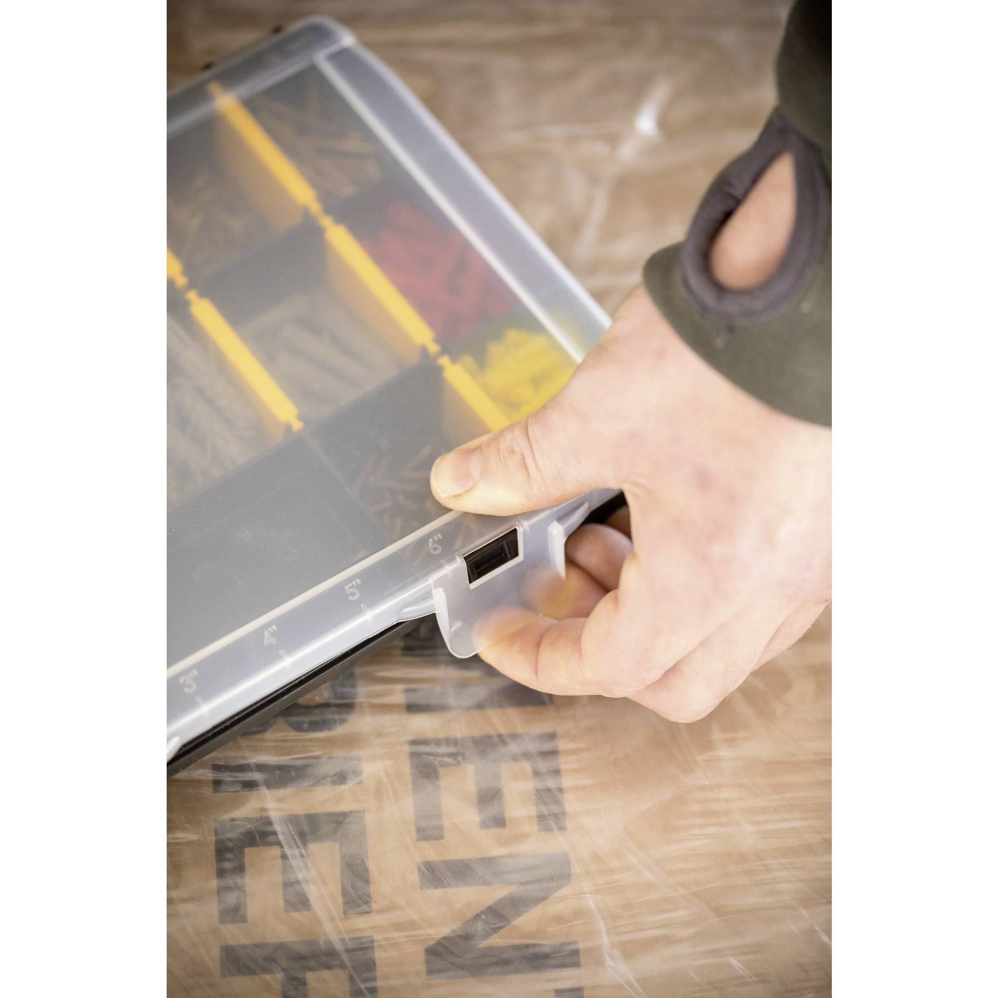 Eine Hand öffnet eine durchsichtige Box mit gelben und schwarzen Fächern, die verschiedene kleine Gegenstände enthält.