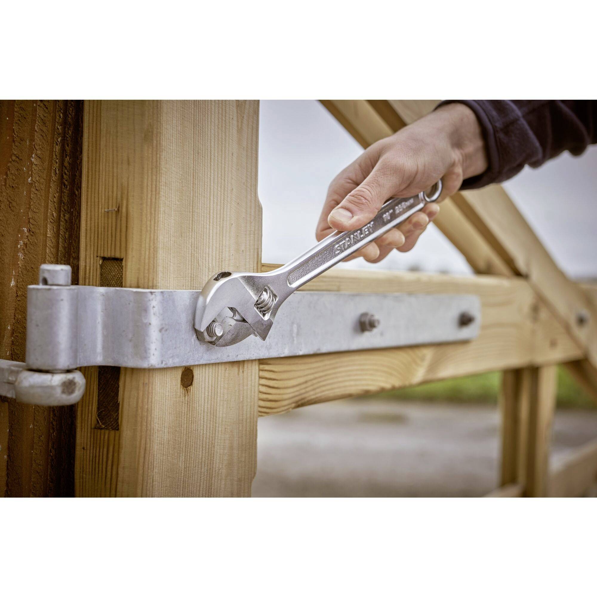 Eine Hand justiert einen Bolzen an einem Holztor mit einem verstellbaren Schraubenschlüssel.