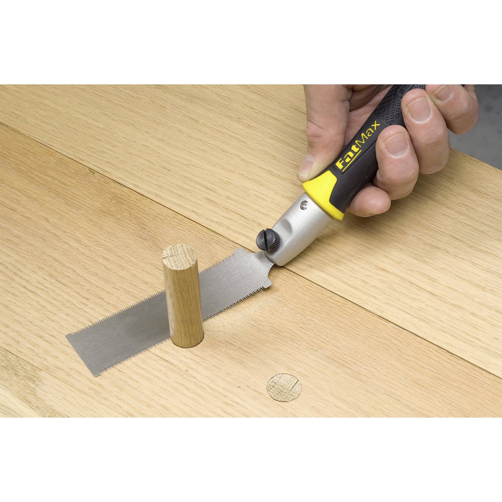 Eine Hand verwendet eine kleine Säge, um einen Holzdübel bündig mit einer Holzoberfläche abzusägen.