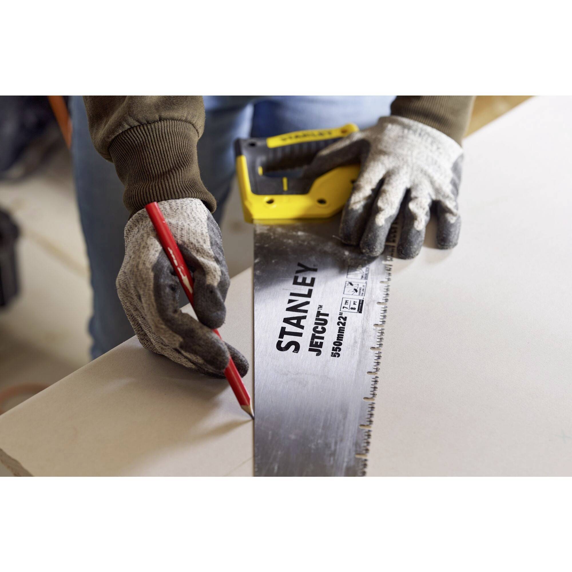 Ein Handwerker zeichnet mit einem roten Stift eine Linie auf Holzmaterial, während er ein Maßband und eine Handsäge hält.