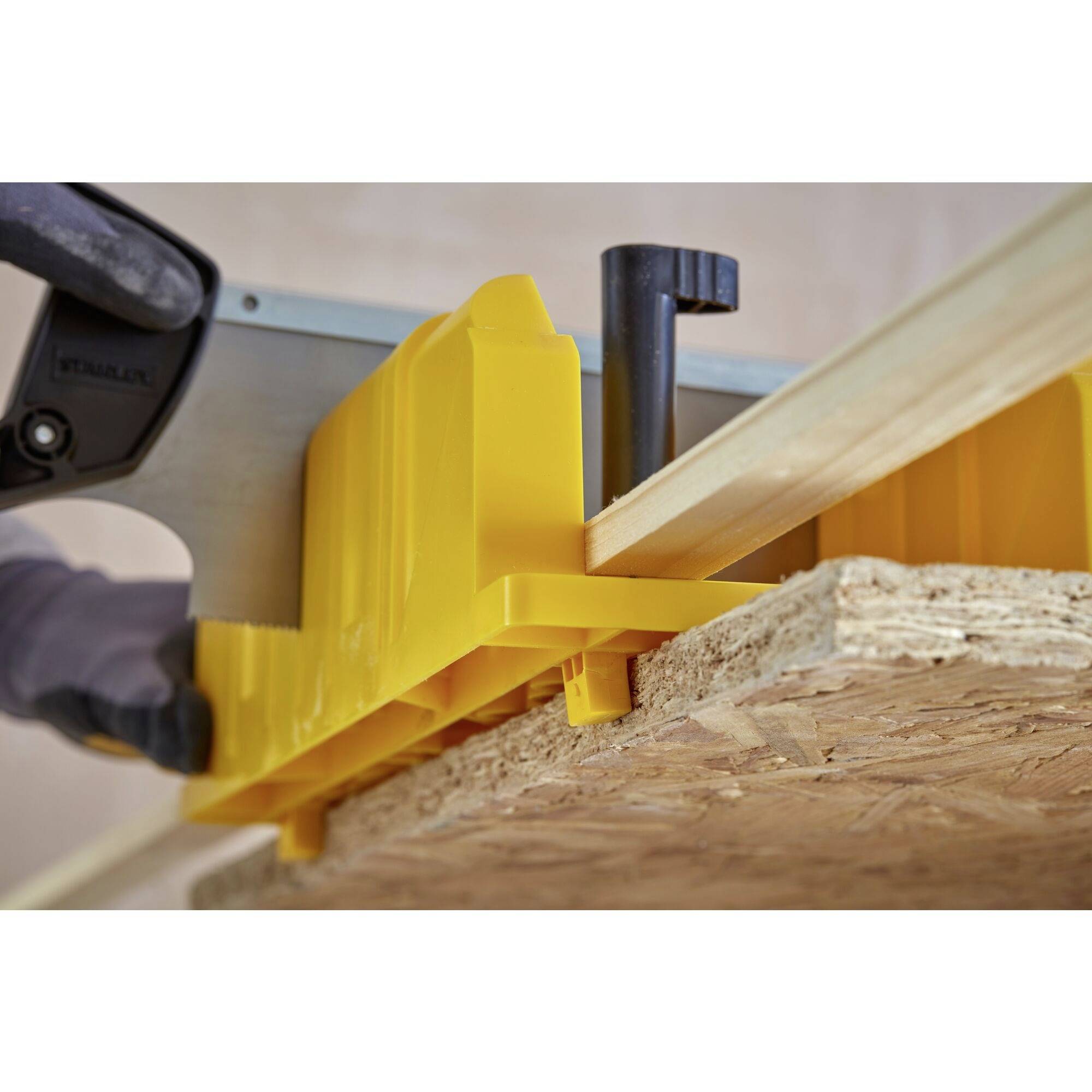 Eine Person schneidet mit einer Handsäge ein Holzbrett. Ein gelber Winkelanschlag ist als Führungshilfe am Holz fixiert.