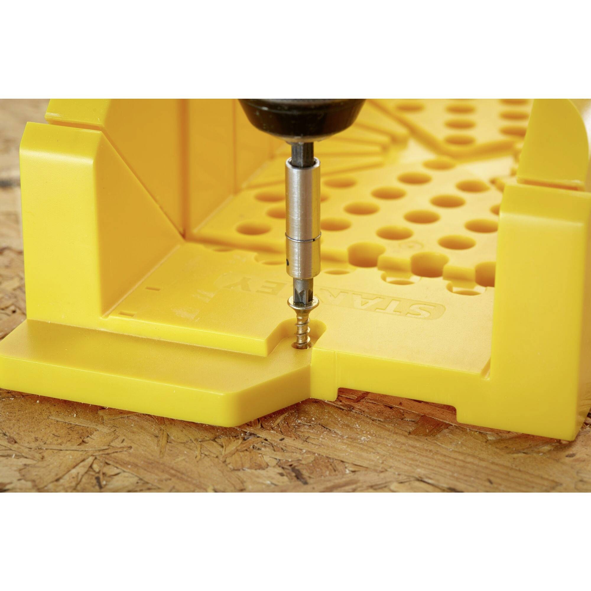 'Nahaufnahme eines gelben Bohrlochteilers auf einer Holzoberfläche. Ein Bohrer wird in eines der Löcher eingesetzt.'