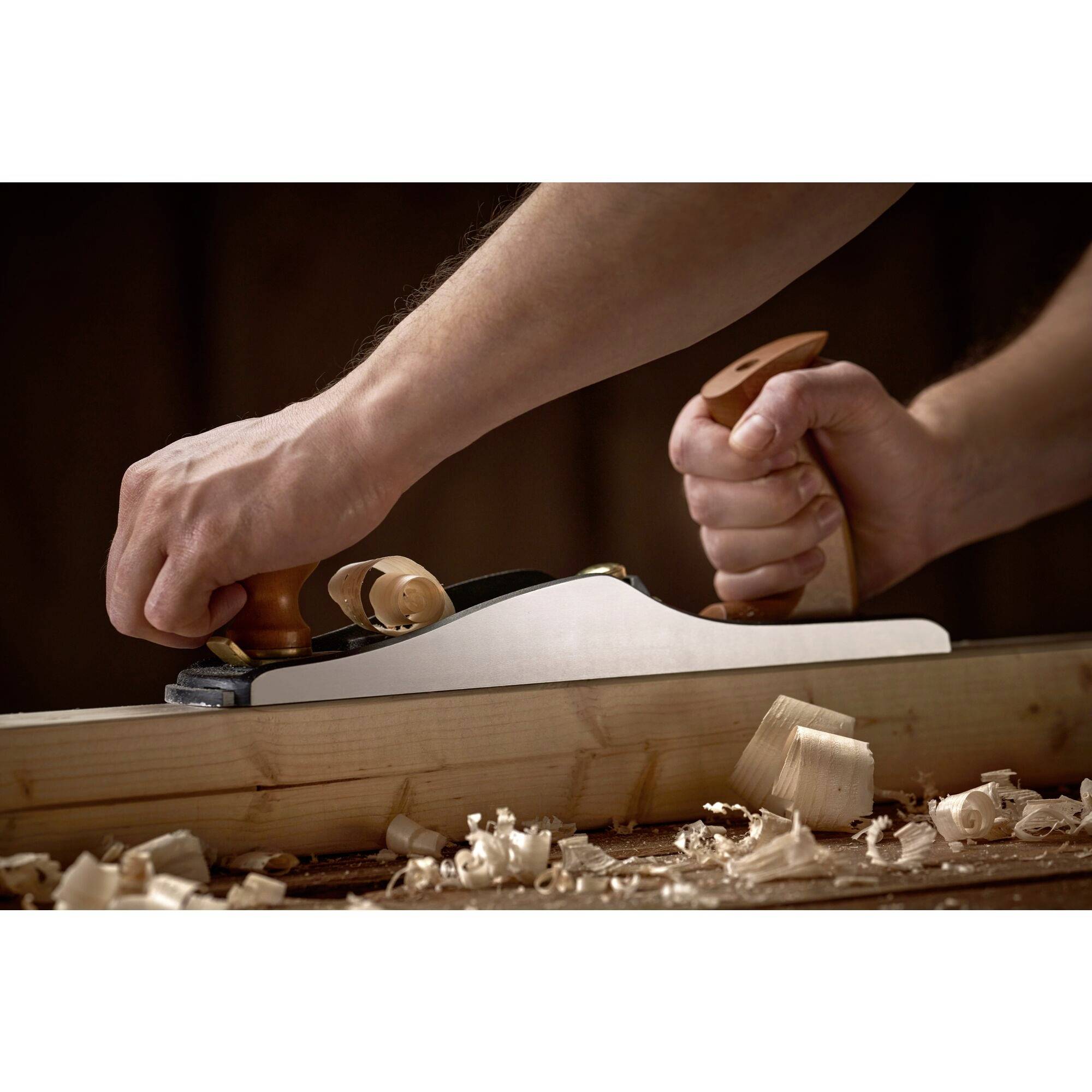 Holzarbeit: Eine Person hobelt mit einem Handhobel über ein Holzbrett, umgeben von Holzspänen.