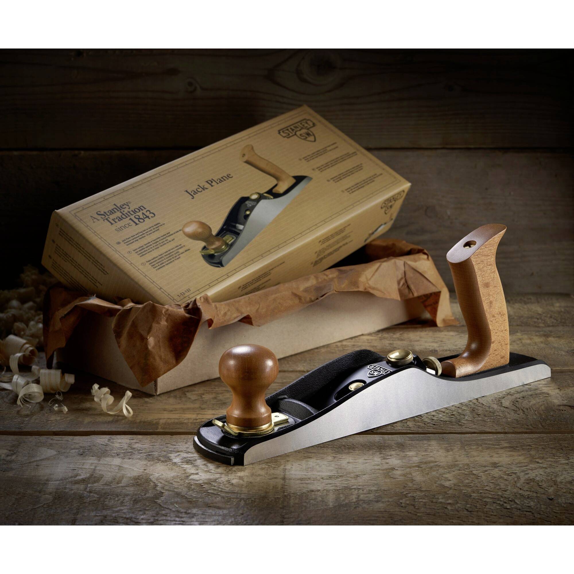 Handhobel aus Holz und Metall auf einem Holztisch, daneben eine geöffnete Verpackung mit Hobelspänen.