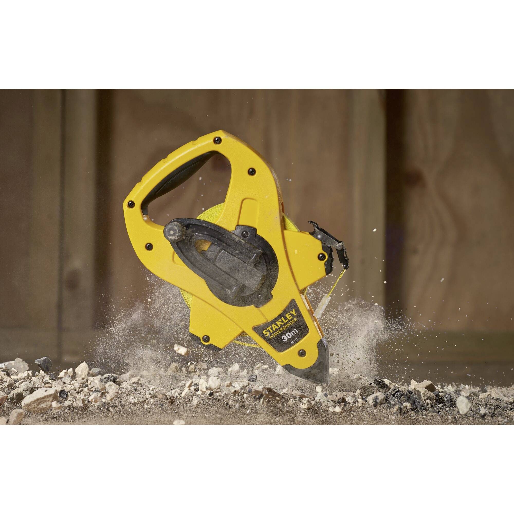 Ein gelbes Maßband von Stanley liegt auf steinigem Boden. Staub und Schutt fliegen, was auf Bewegung oder kürzliche Nutzung hindeutet.