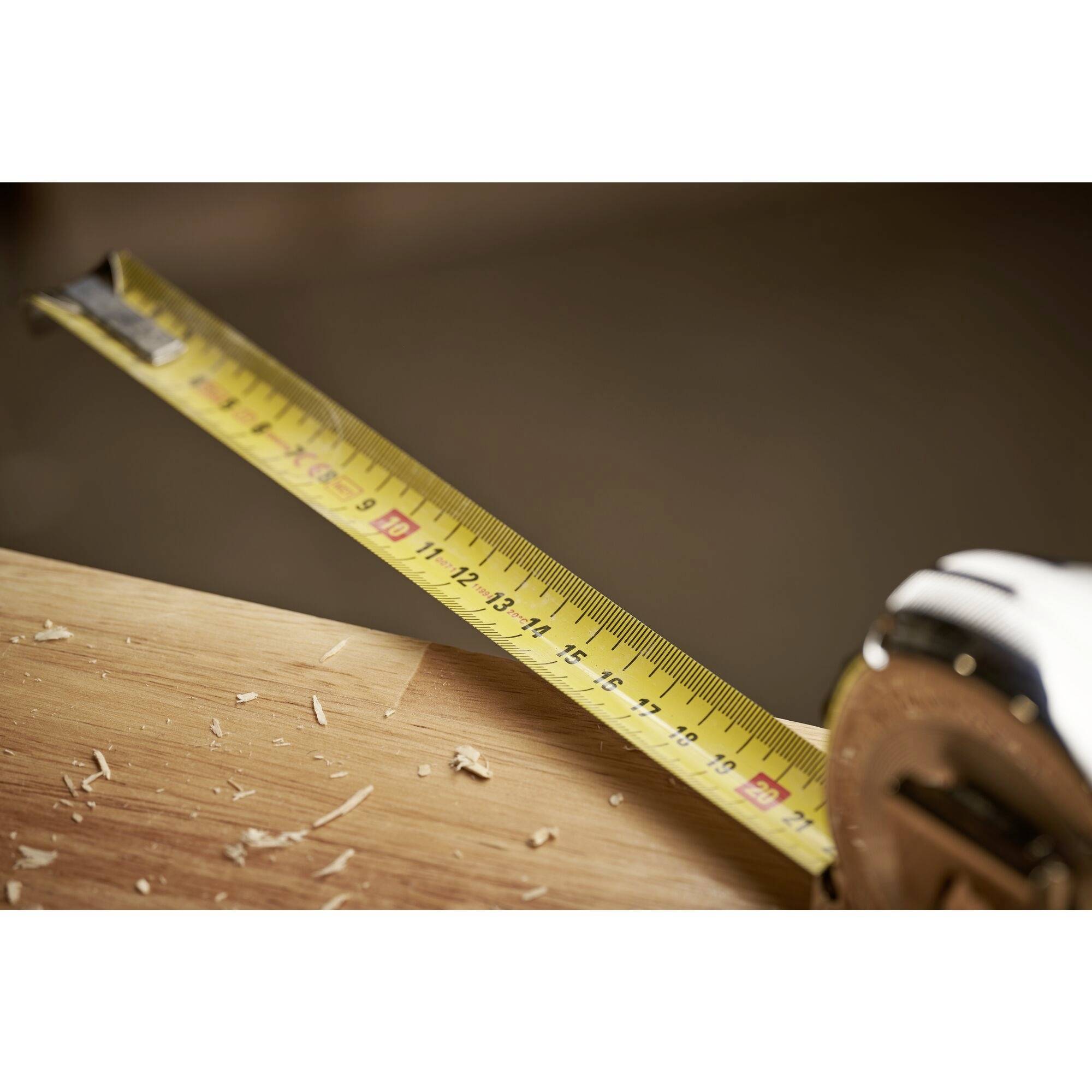 Ein ausgerolltes Maßband liegt auf einem Holztisch, umgeben von Holzspänen. Es zeigt eine Länge von etwa 15 Zentimetern an.