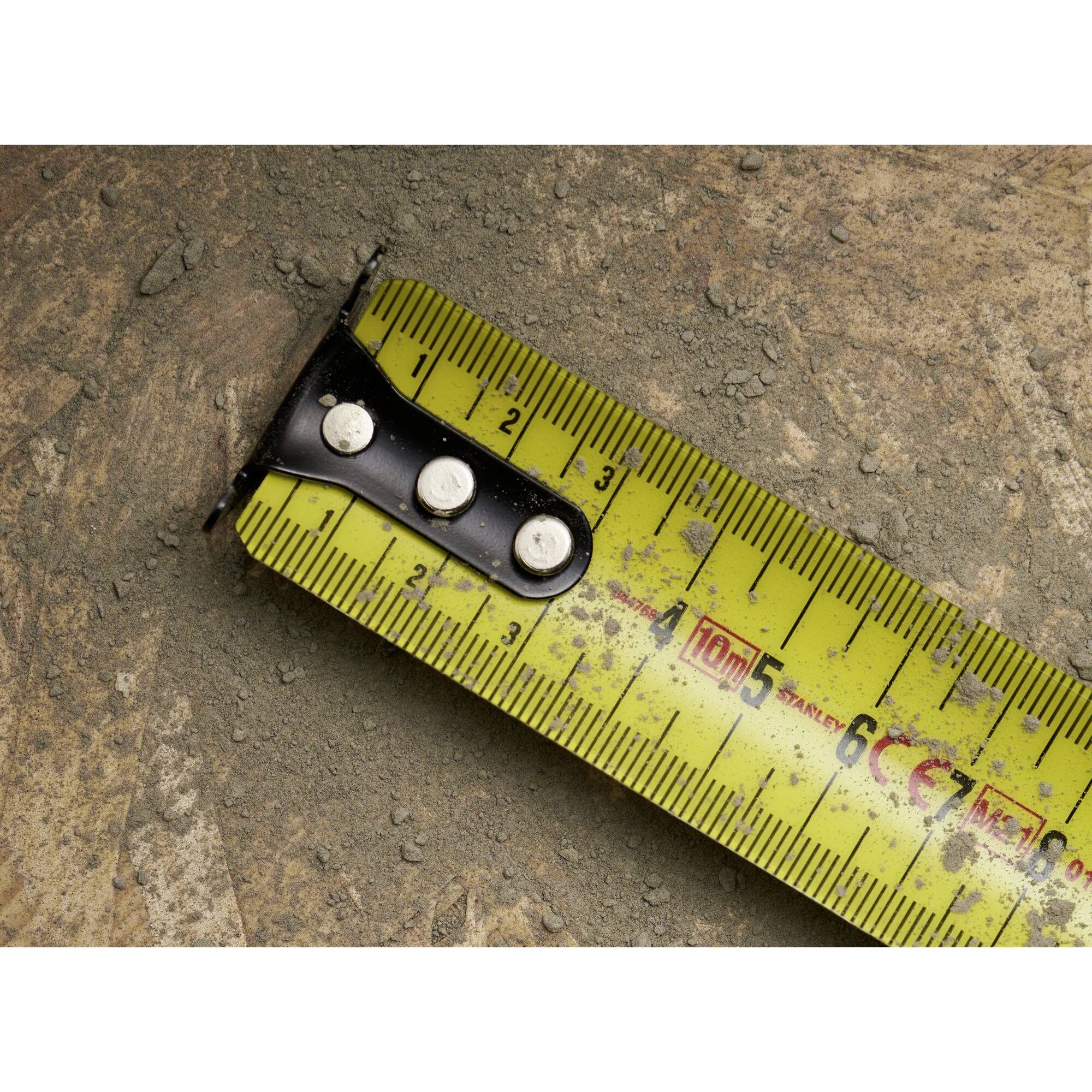 Ein gelbes Maßband auf staubigem Boden misst 20 cm, zeigt handwerkliche Arbeit oder Bauaktivität.