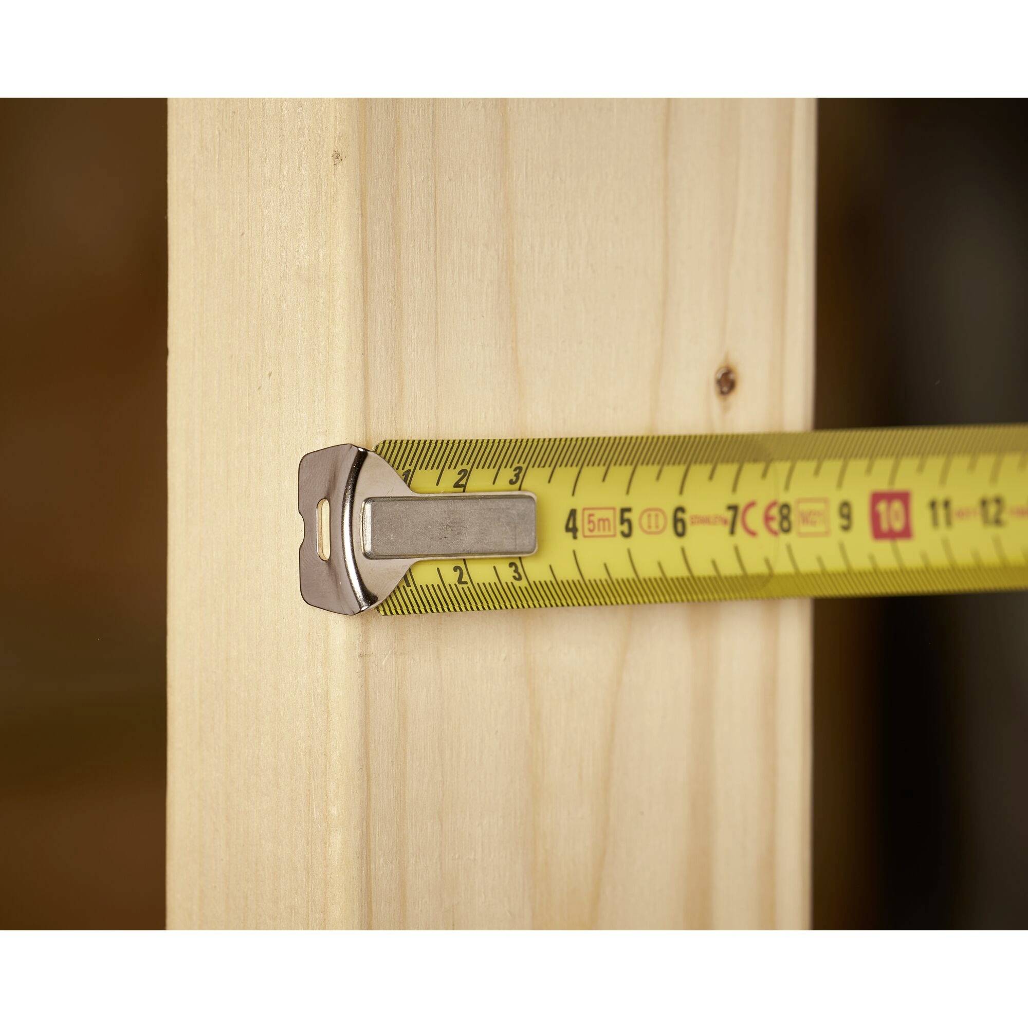Ein Maßband misst ca. 3 cm an einem Holzbrett. Das Bild illustriert Genauigkeit beim Messen von Materialien für handwerkliche Arbeiten.