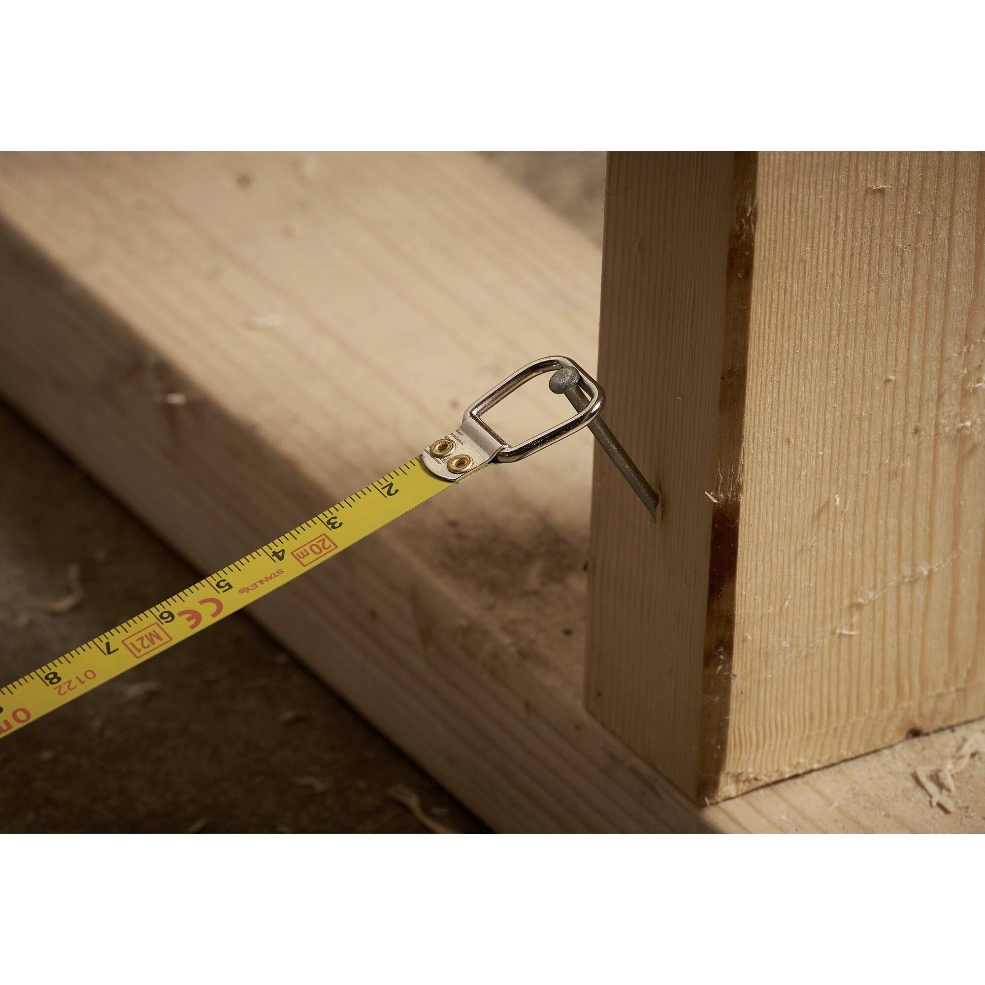 Ein Maßband misst die Breite eines Holzbretts, das auf einem Boden liegt. Es zeigt eine Breite von etwa 2,5 cm an.