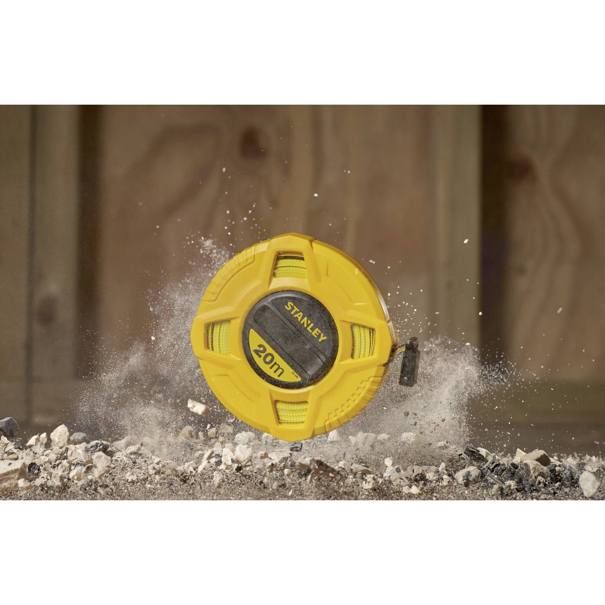 Ein gelbes Maßband liegt auf Schutt, umgeben von Staub und Trümmern, auf einem Baustellenhintergrund.