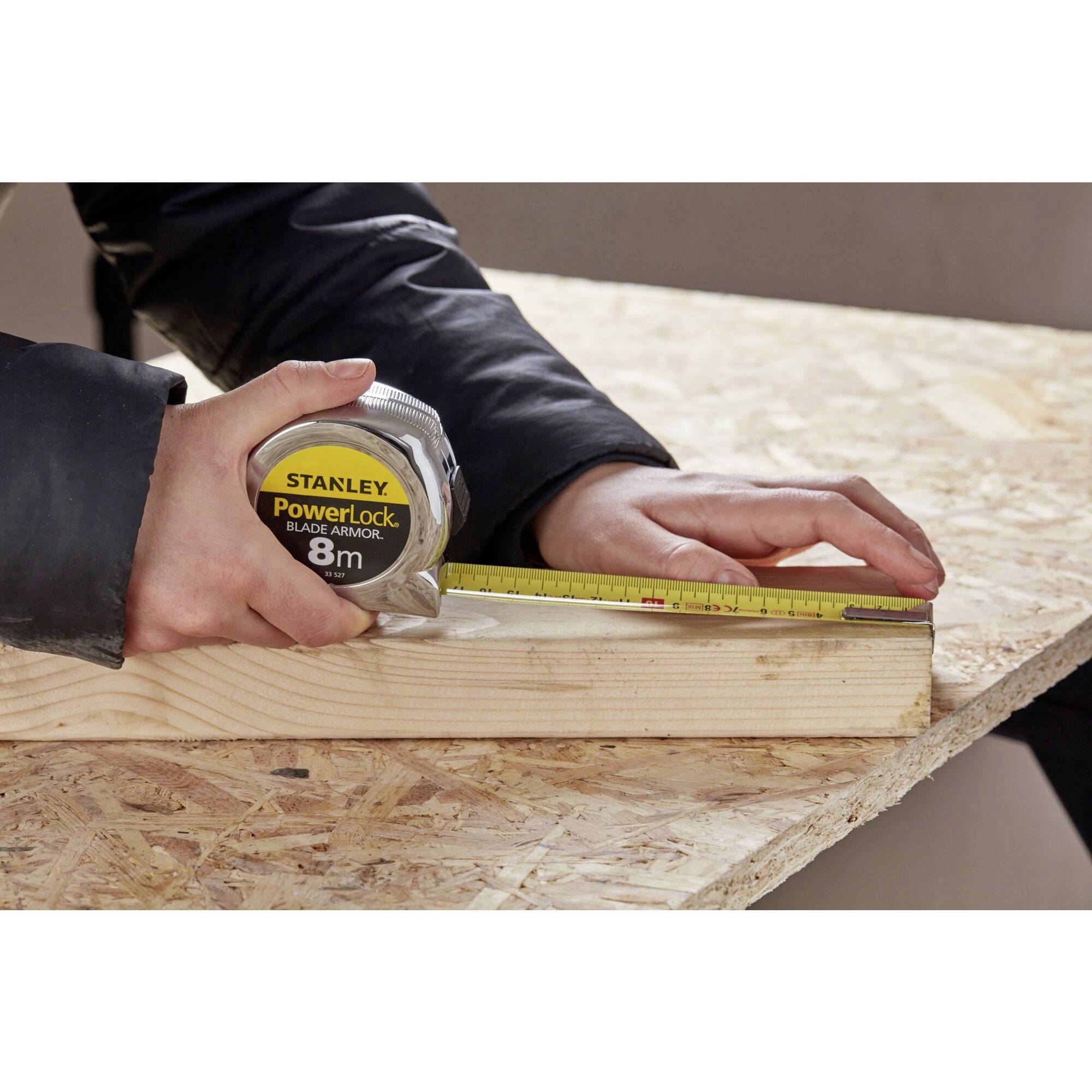 Person misst ein Holzstück mit einem Maßband auf 8 cm Länge.