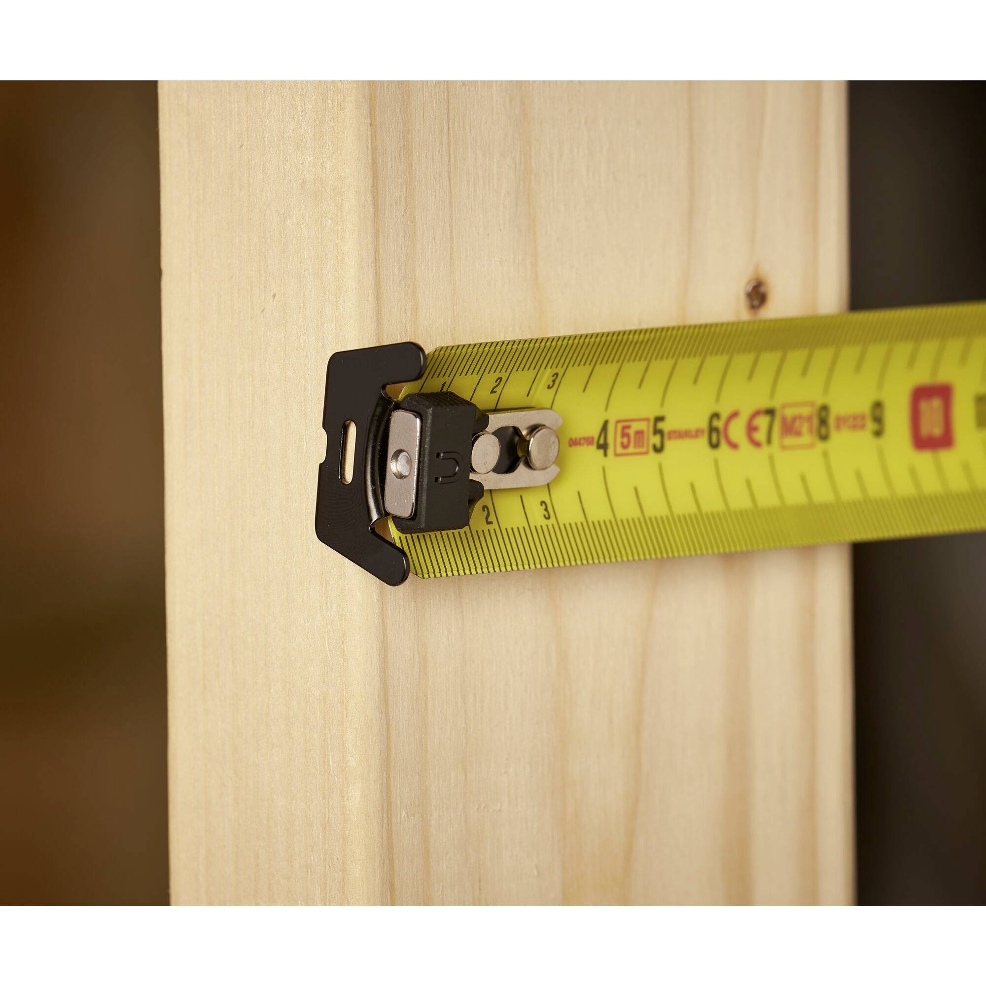 Ein Maßband misst ein Holzbrett und zeigt eine Länge von etwa 5 Zentimetern an. Das Brett hat eine glatte, helle Oberfläche.