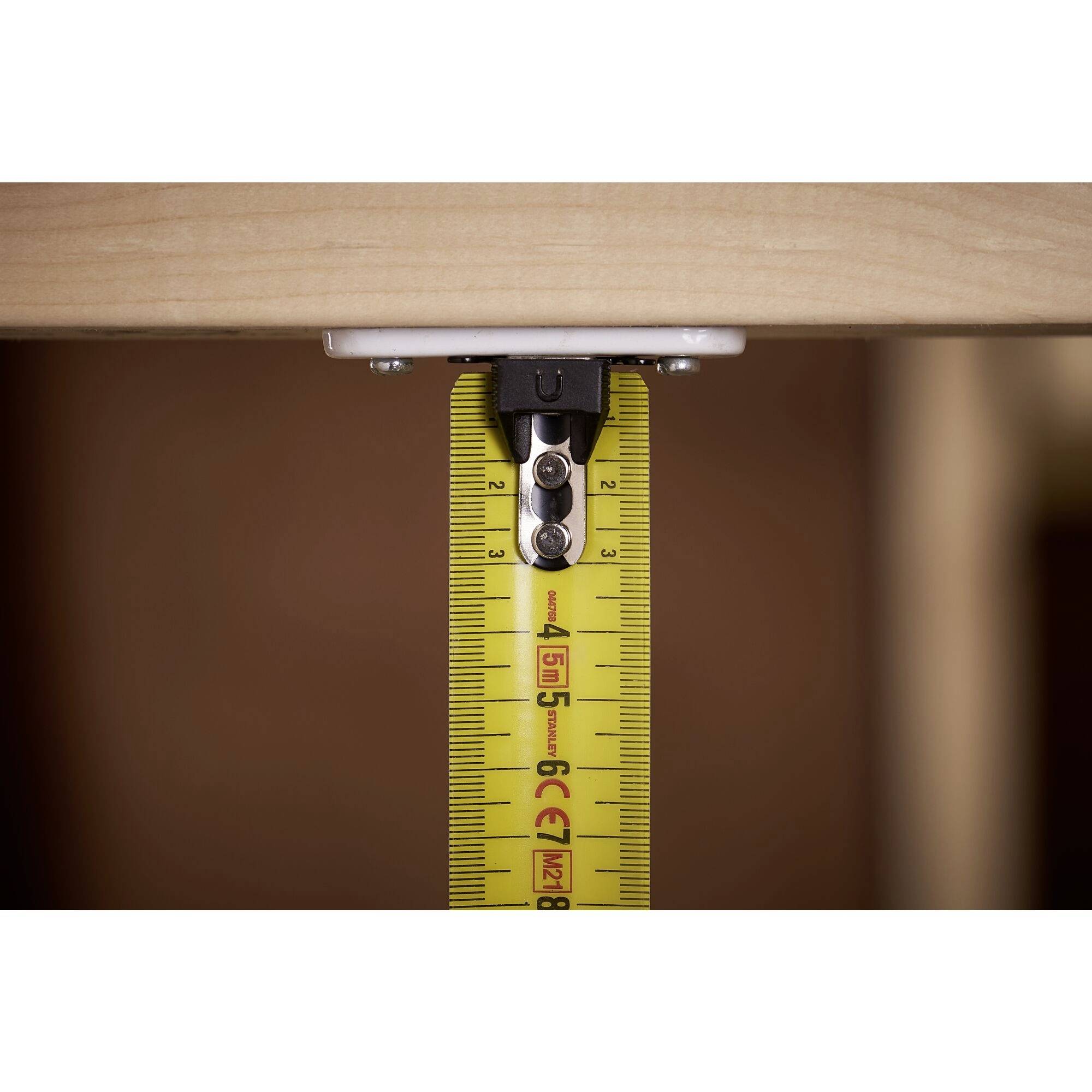 Ein Maßband wird an einem Holzrahmen gehalten, zeigt eine Länge von etwa 45 cm an. Es misst den Abstand für Bau- oder Möbelprojekte.