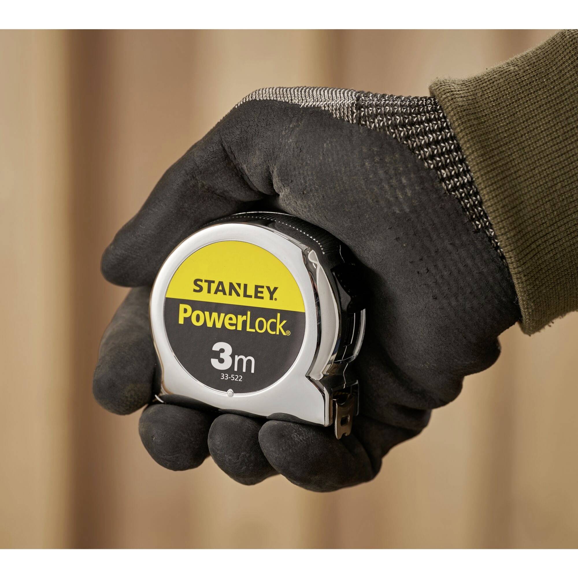 Eine Hand hält ein Stanley PowerLock Maßband mit 3 m Länge.