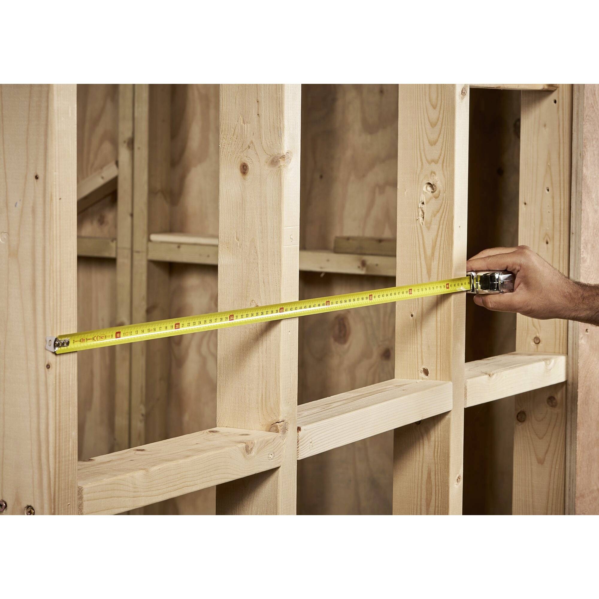 Ein Maßband wird an einem Holzrahmen angelegt, um eine präzise Länge zu messen. Hauptfokus liegt auf der genauen Vermessung.