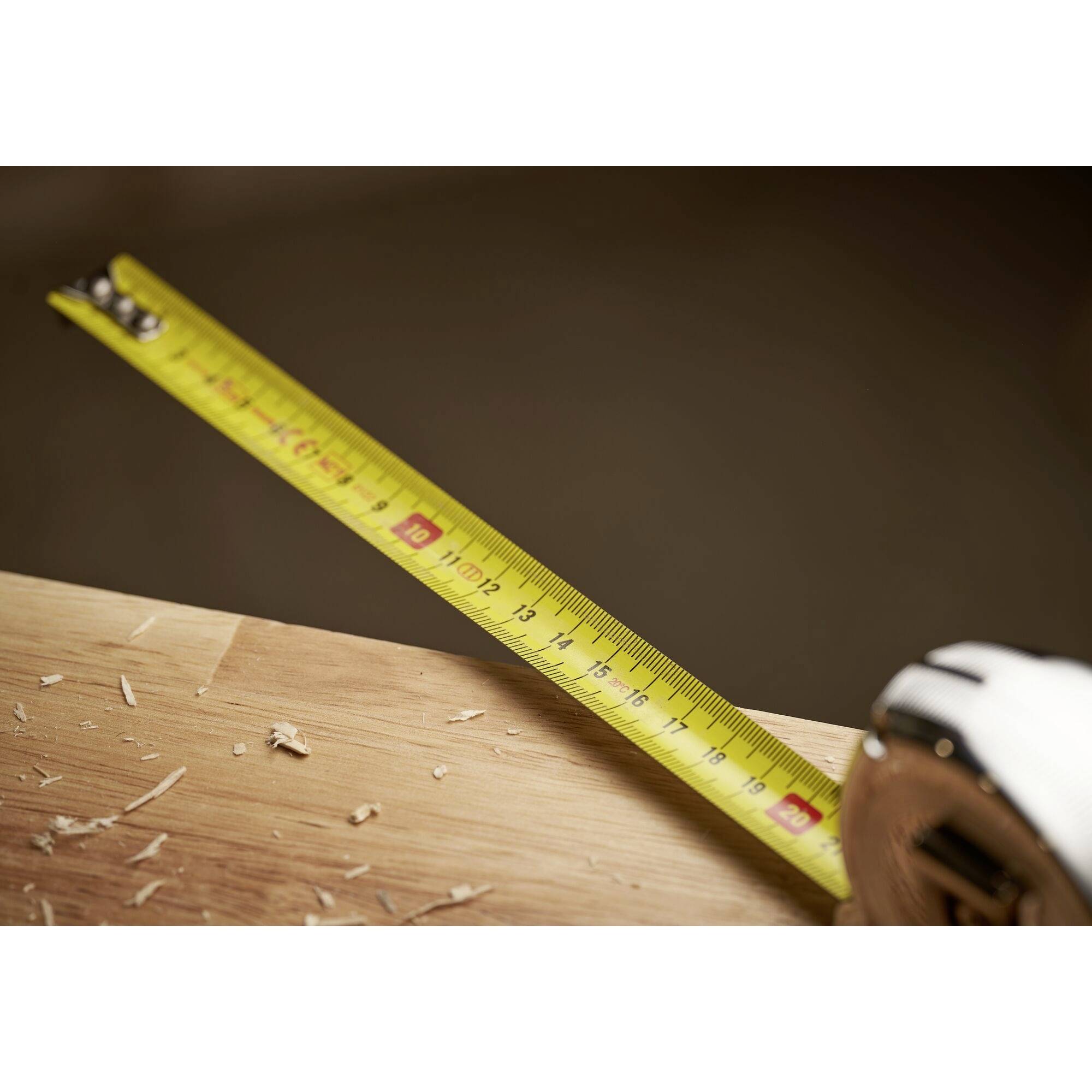 Ein Maßband wird über ein Stück Holz mit Holzspänen gespannt, zeigt eine Länge von etwa 30 cm.