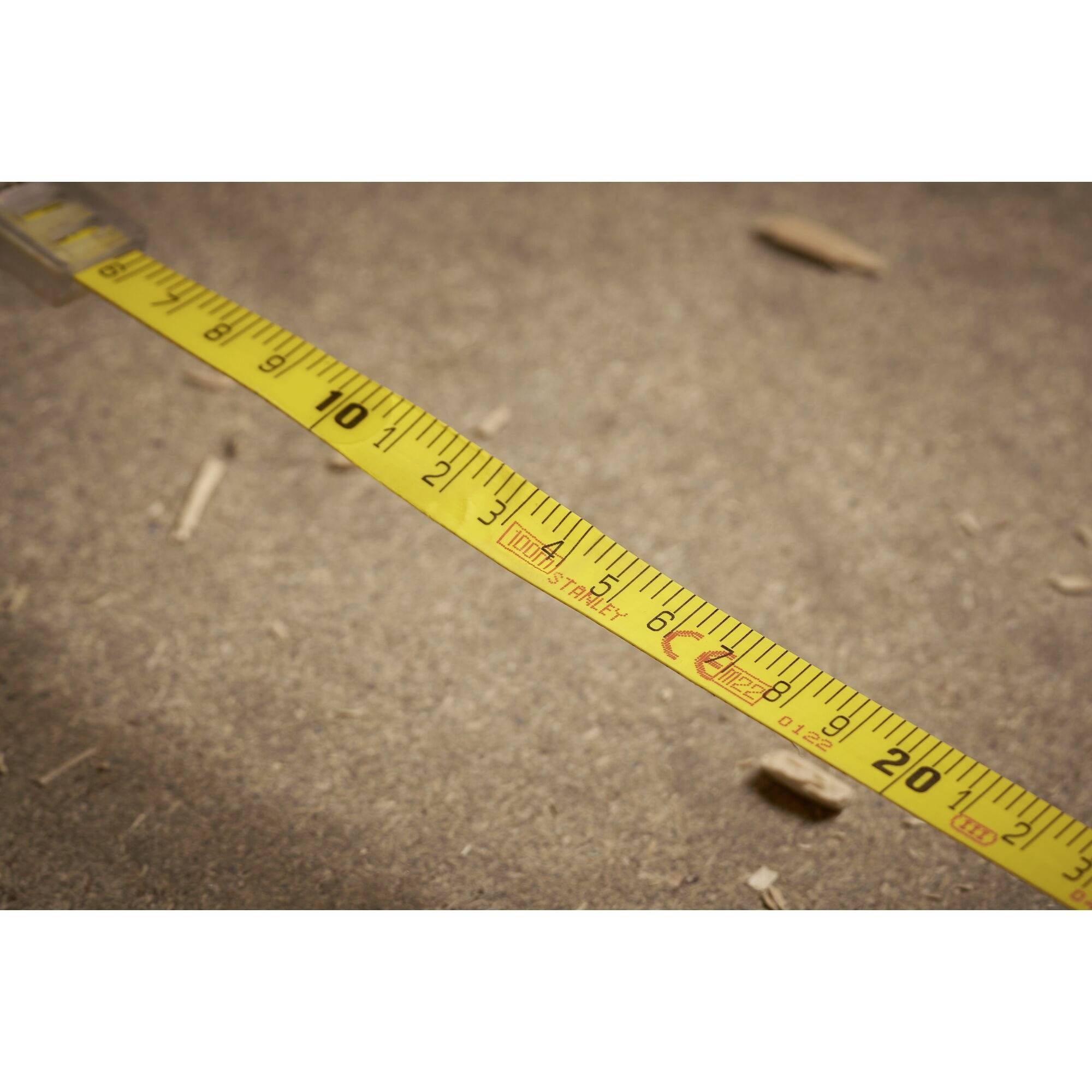 Gelbes Maßband auf einem braunen Boden, zeigt centimeter Markierungen bis 250. Verwendet im Bau oder Heimwerken zur genauen Messung.
