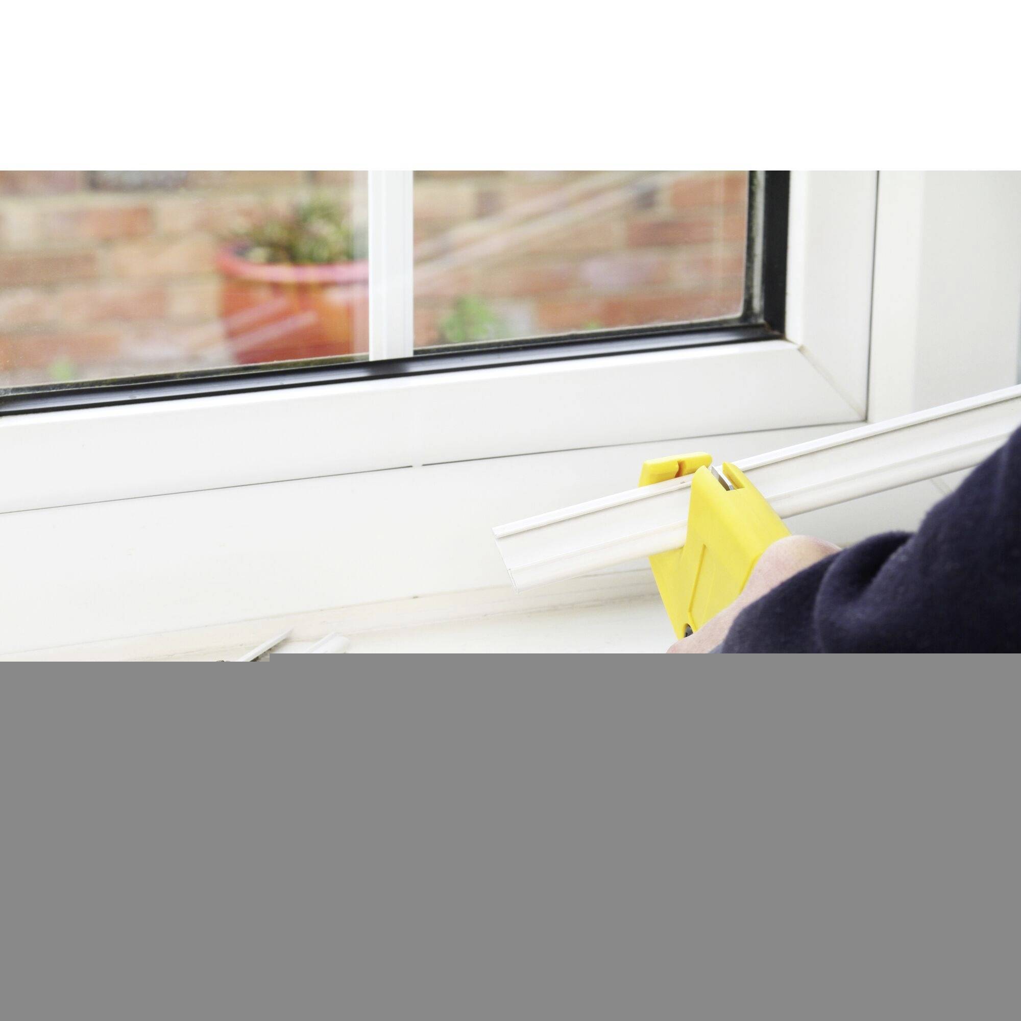 Person verwendet eine gelbe Werkzeugpistole, um eine weiße Dichtung an einem Fensterrahmen anzubringen.