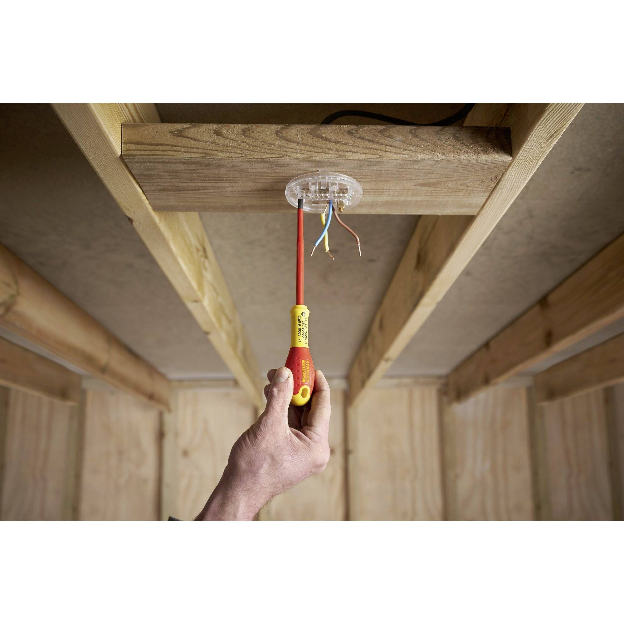 Eine Person installiert eine Deckenleuchte in einem Holzrahmenbau. Ein Schraubendreher wird verwendet, um Drähte anzuschließen.