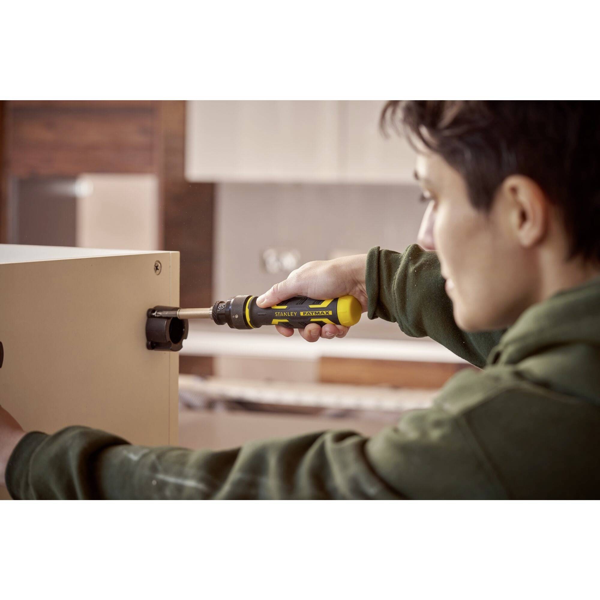 Eine Person befestigt eine Schraube an einem Möbelstück mit einem gelb-schwarzen Schraubendreher in einer häuslichen Umgebung.