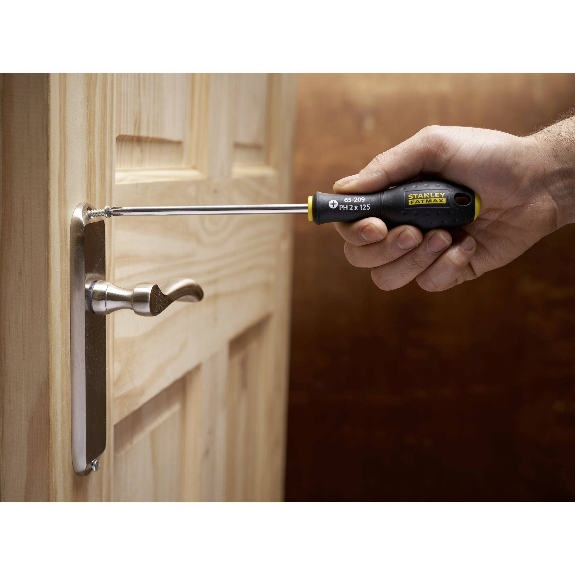 Eine Hand, die einen Schraubendreher benutzt, um eine Schraube in ein Türscharnier einzudrehen. Holztür im Hintergrund.