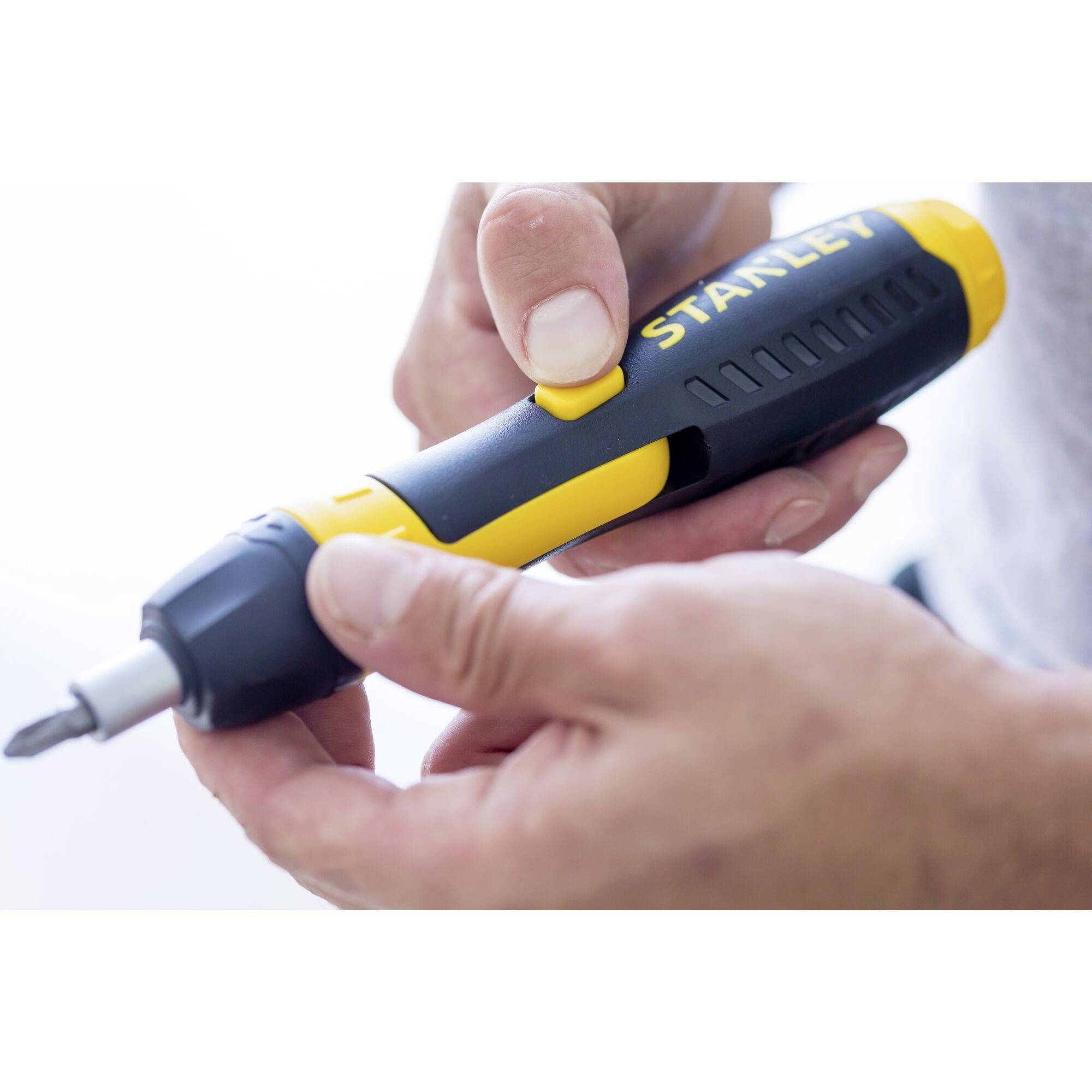 Ein Hand hält einen gelb-schwarzen Akku-Schraubendreher mit der Aufschrift 'Stanley'. Eine Person justiert die Drehgeschwindigkeit.