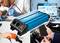 Männer arbeiten mit Elektronik und Werkzeugen. Ein blauer Voltcraft Spannungswandler ist im Vordergrund. Grafiken im Hintergrund.
