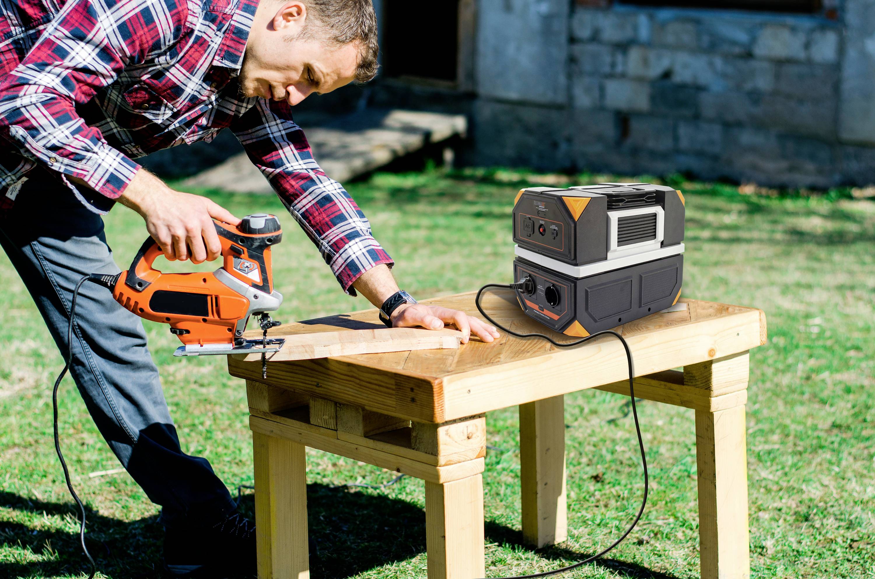 Person sägt Holz auf einem Tisch im Freien. Ein tragbarer Stromgenerator versorgt das Elektrowerkzeug mit Energie.