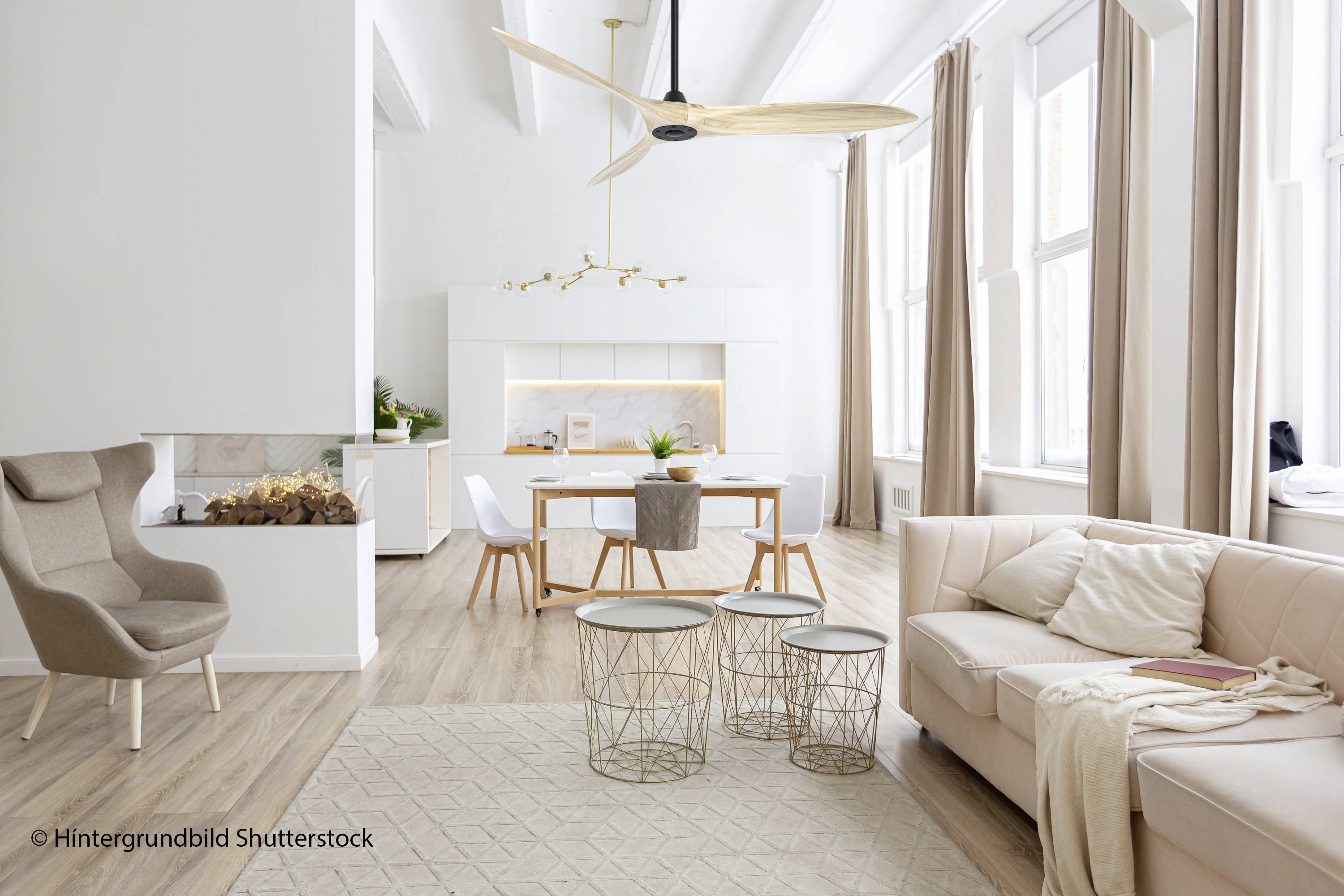 Helles Wohnzimmer mit beigem Sofa, modernem Sessel, drei runden Tischen und offener Küche im Hintergrund. Luftig und minimalistisch gestaltet.
