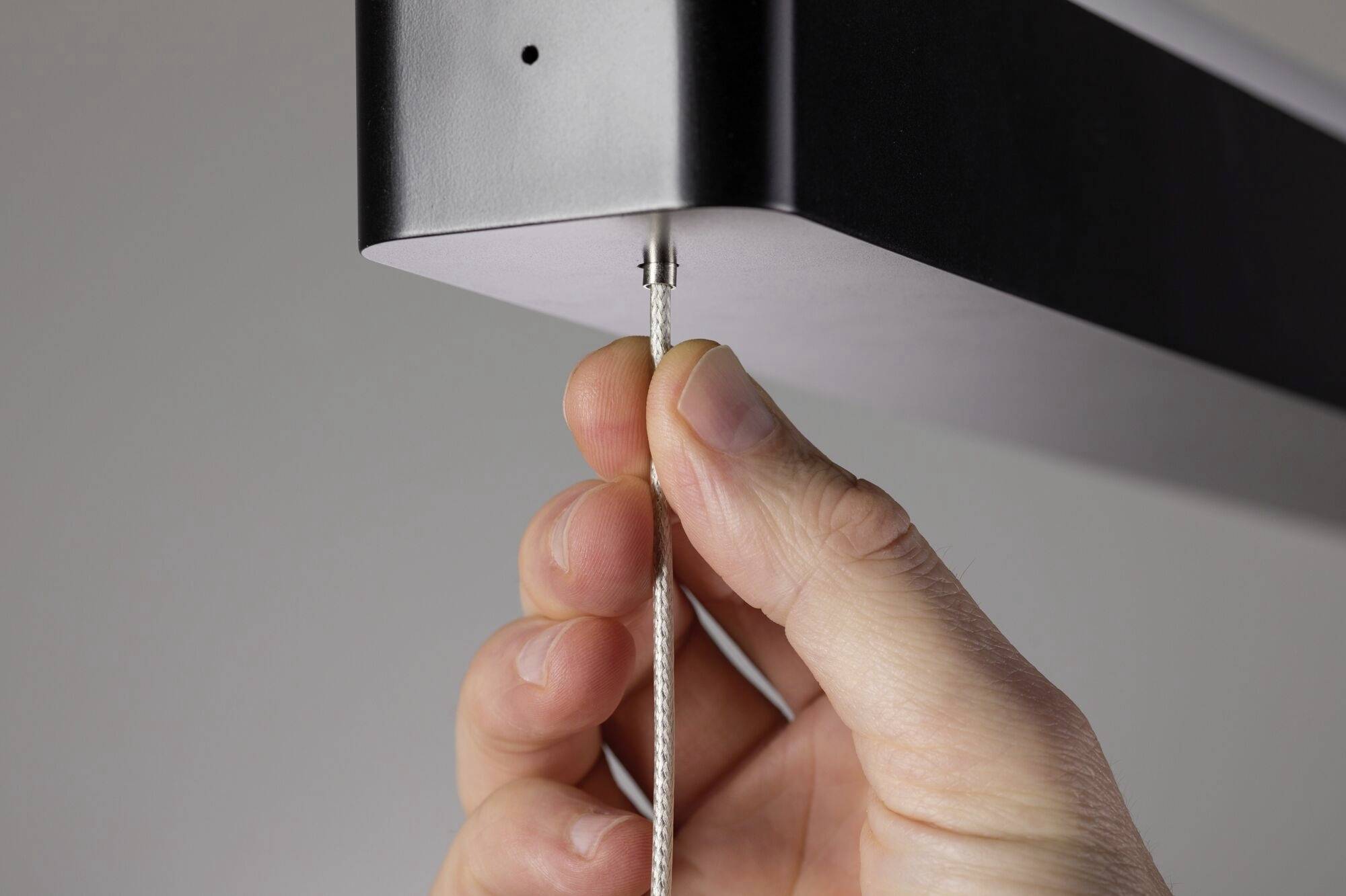 Eine Hand zieht an einem dünnen Kabel, das mit der Unterseite eines rechteckigen Geräts verbunden ist.