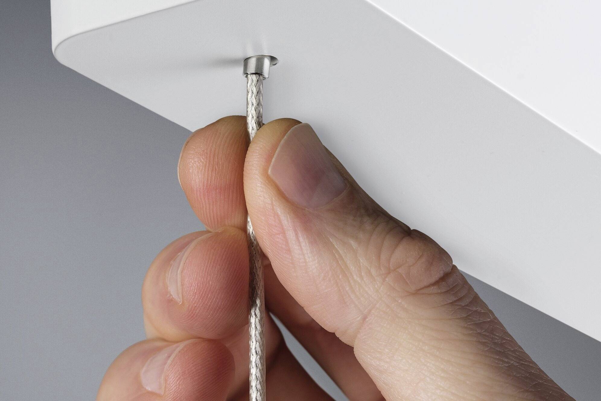 Eine Hand zieht an einem dünnen Kabel, das aus einem weißen Gehäuse kommt.