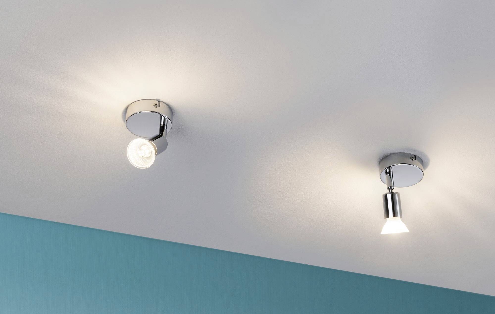 Zwei Deckenleuchten mit modernen, chromfarbenen Fassungen an der Decke, leuchten ein helles, diffuses Licht auf eine blaue Wand.
