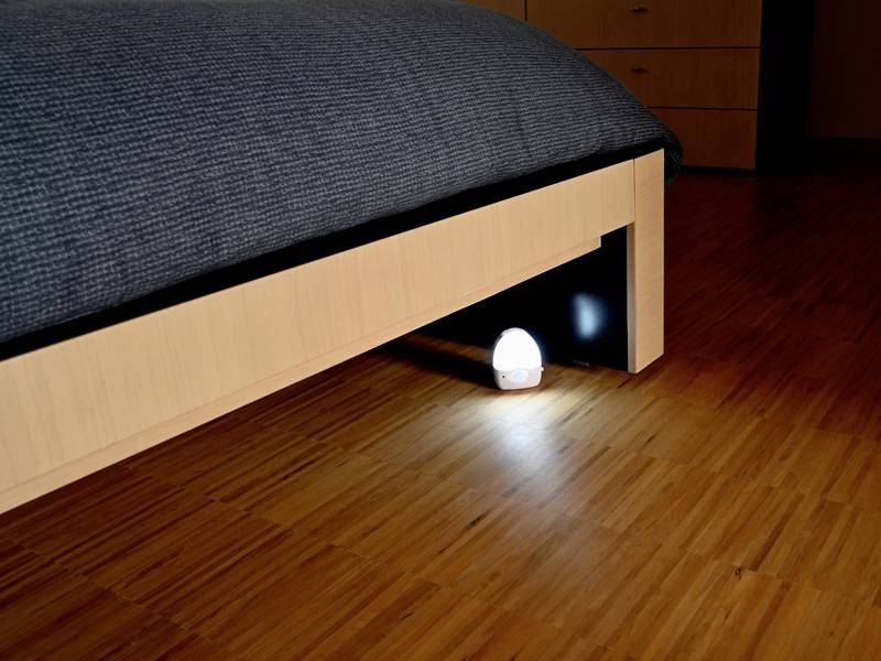 Ein kleines Nachtlicht leuchtet unter einem modernen Holzbett auf hellem Holzboden, erzeugt eine warme Atmosphäre im Schlafzimmer.