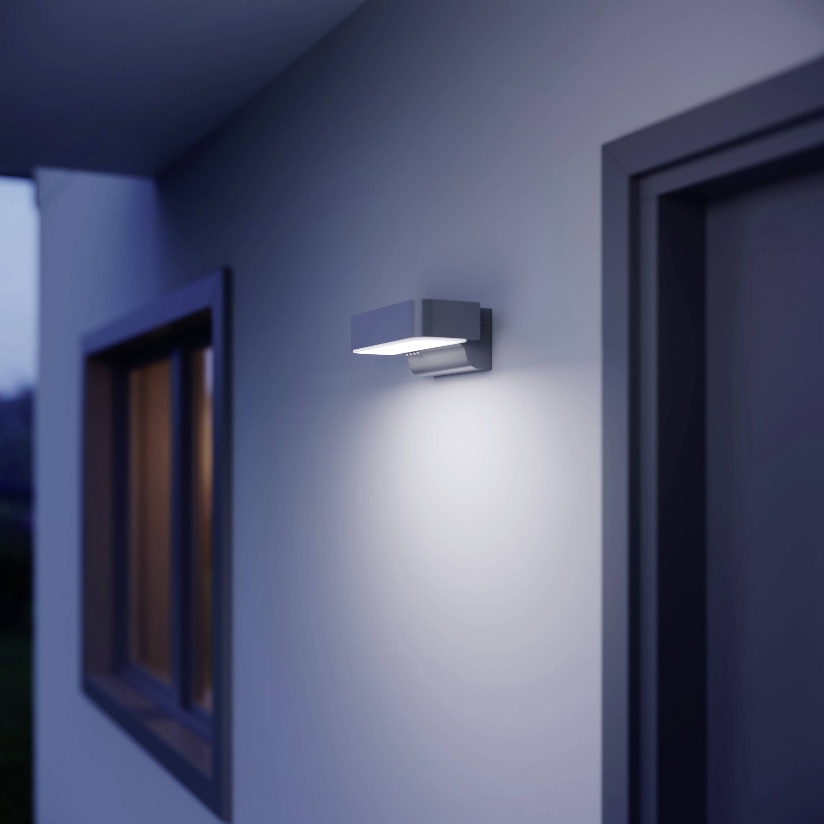 Moderne Außenleuchte an einer Wand, beleuchtet den Eingang eines Hauses in der Dämmerung.