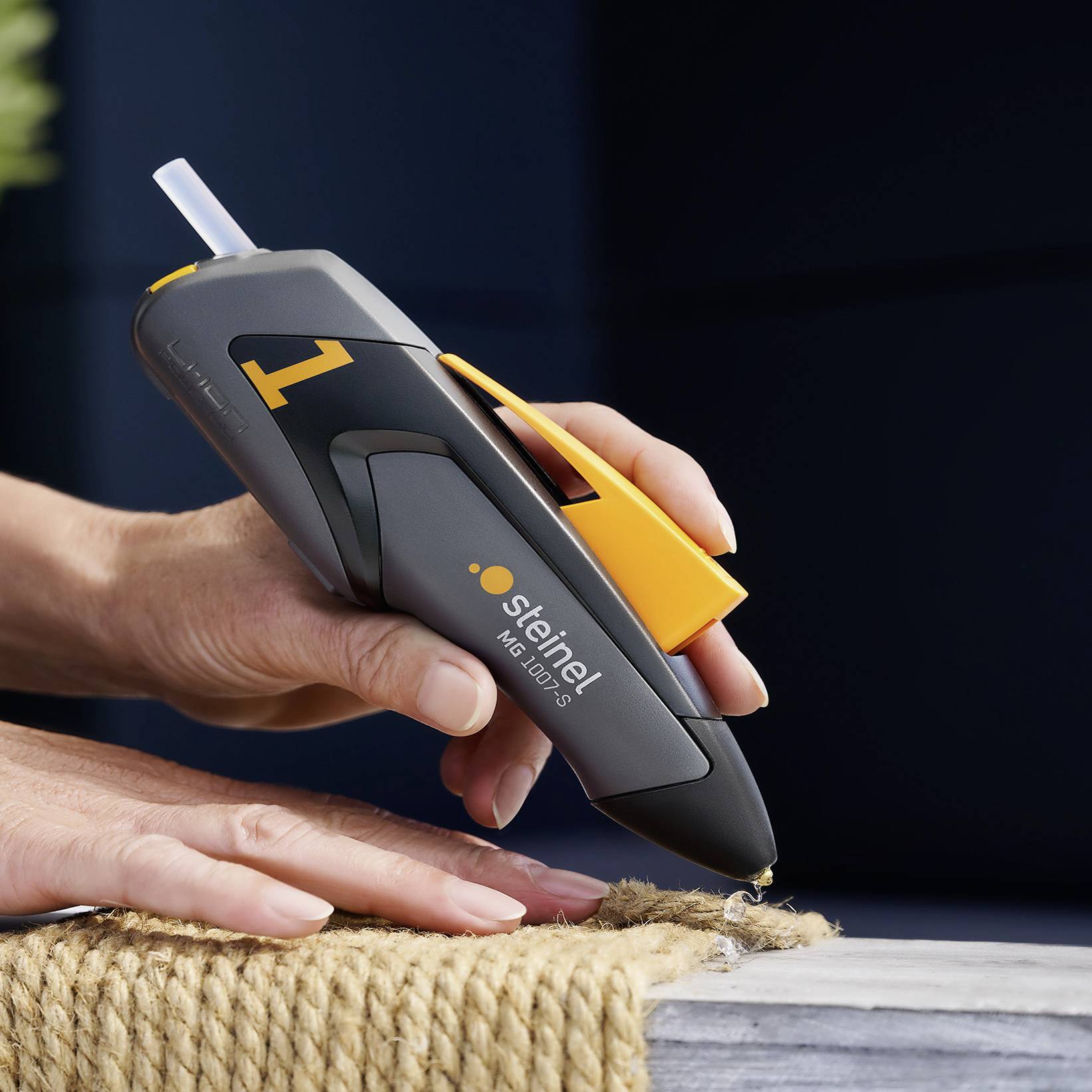 Eine Person verwendet eine schwarze Heißklebepistole von Steinel, Modell 'Neo 1', um ein Seil auf einer grauen Oberfläche zu befestigen.