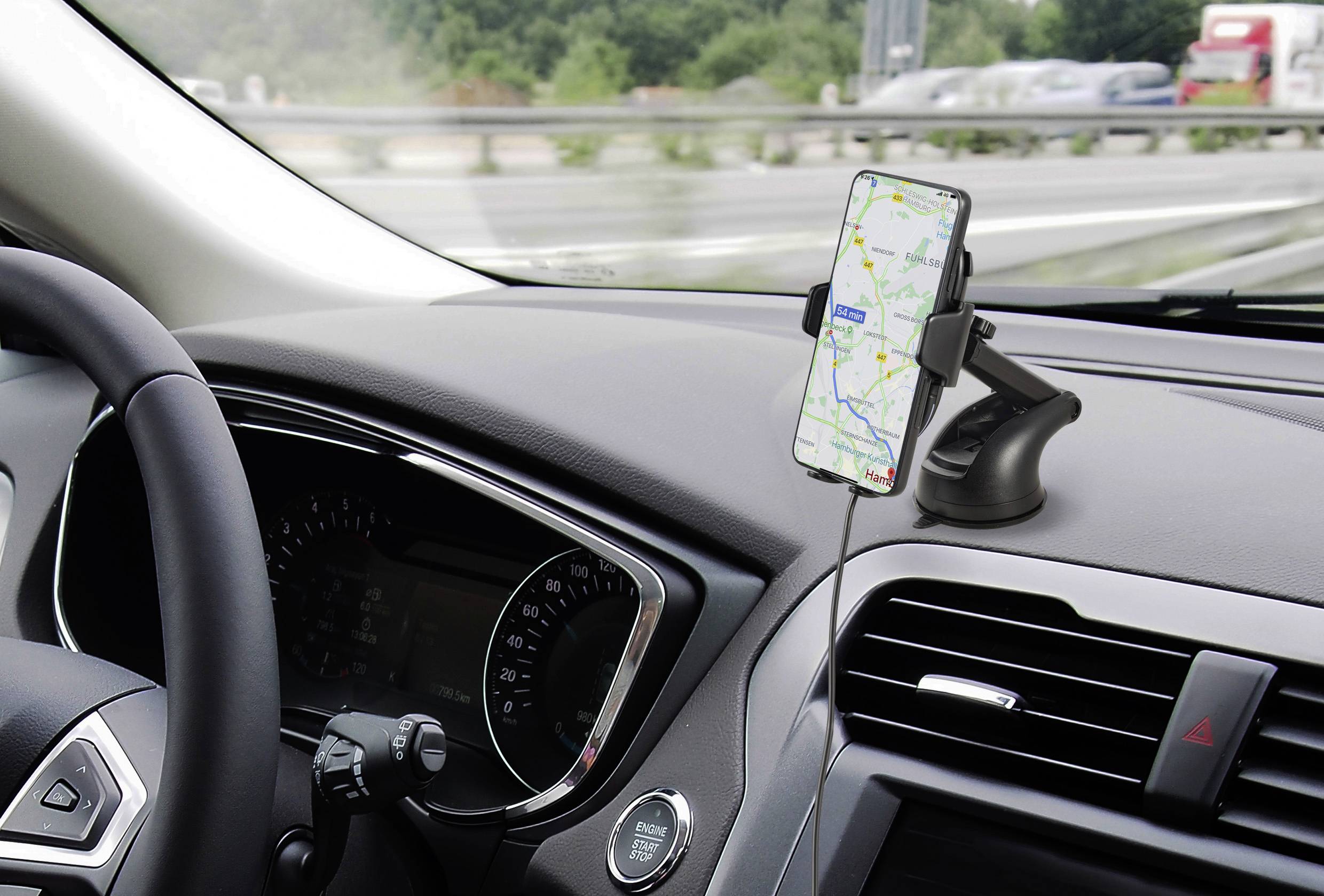 Ein Smartphone mit Navigations-App ist in der Halterung auf dem Armaturenbrett eines Autos, Straße und grüne Landschaft im Hintergrund.